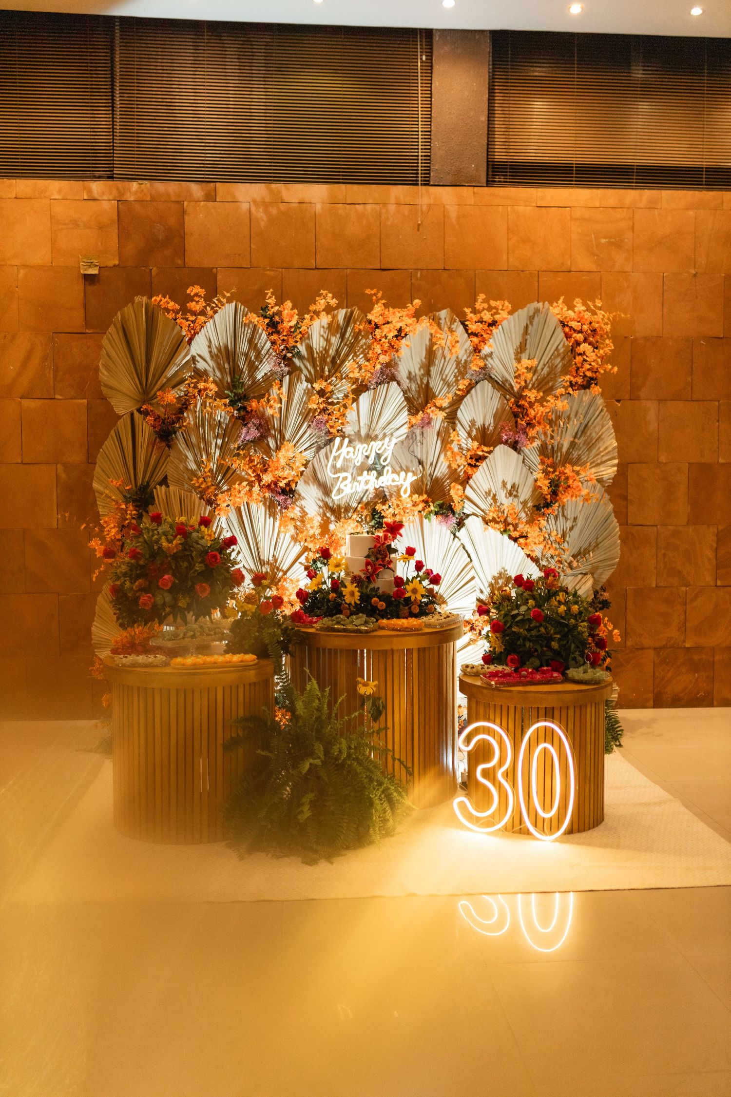 Elegant 30th birthday party decor with floral wall, neon number, gold pedestals, and warm ambient lighting.