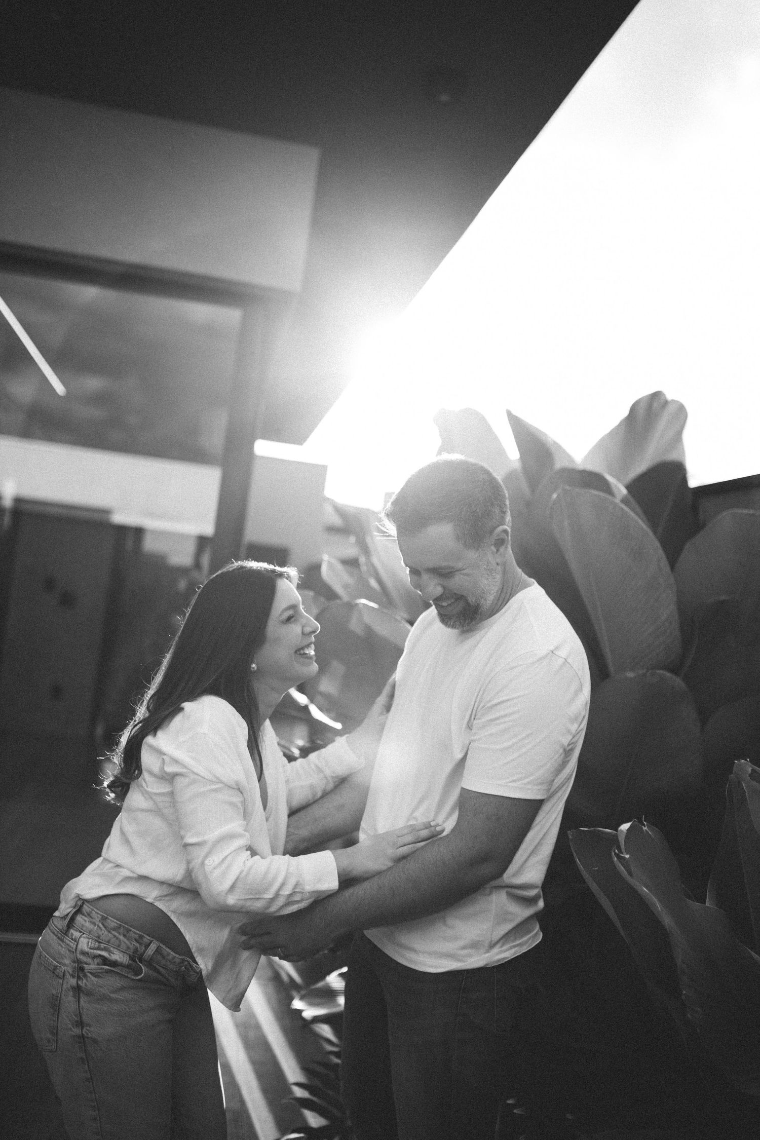 Black and white photo of happy couple embracing and laughing together in warm backlit sunset setting.