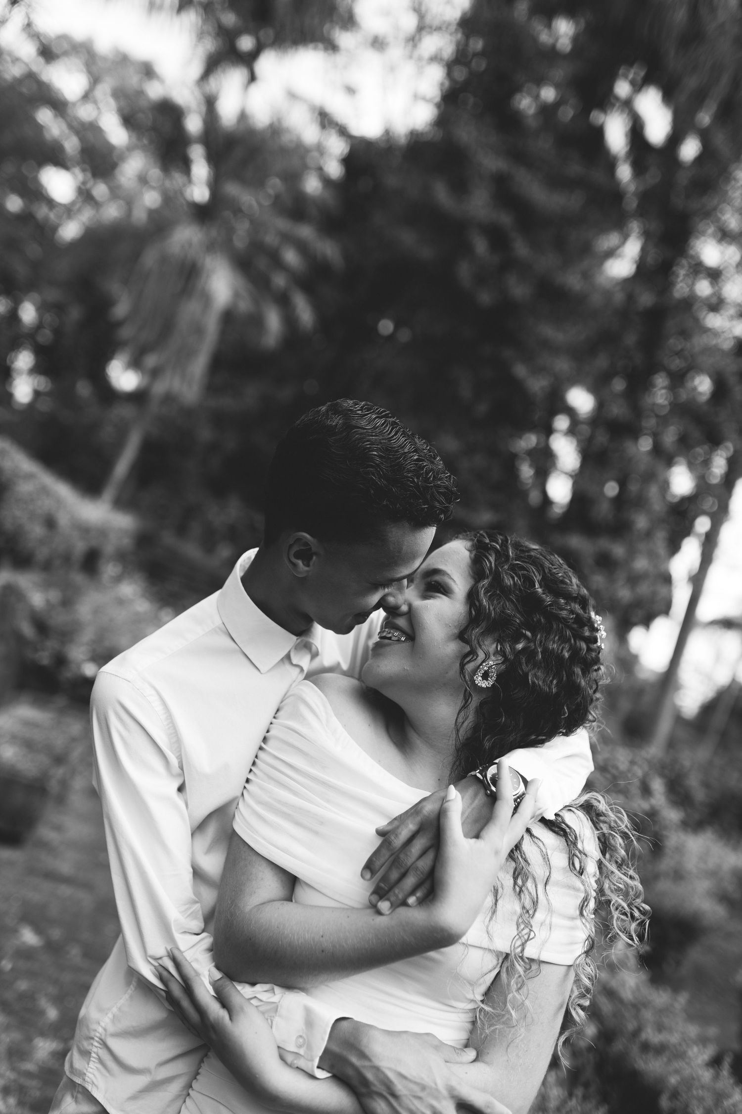 Black and white romantic photo of a smiling couple embracing and almost kissing in a garden setting.