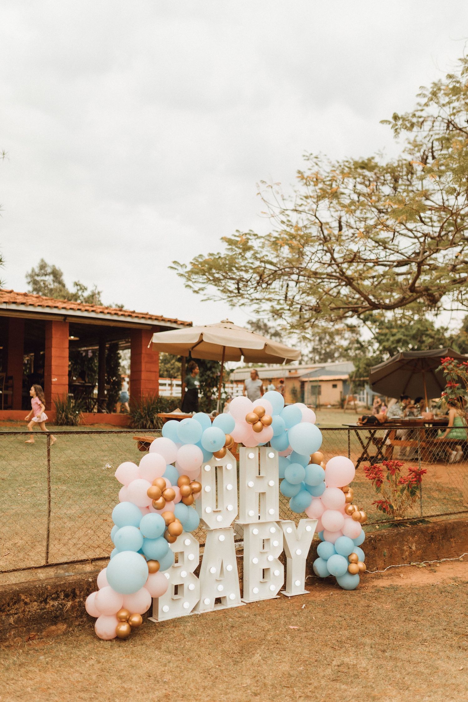Outdoor gender reveal party decoration featuring illuminated OH BABY marquee letters surrounded by blue, pink, and gold balloons.