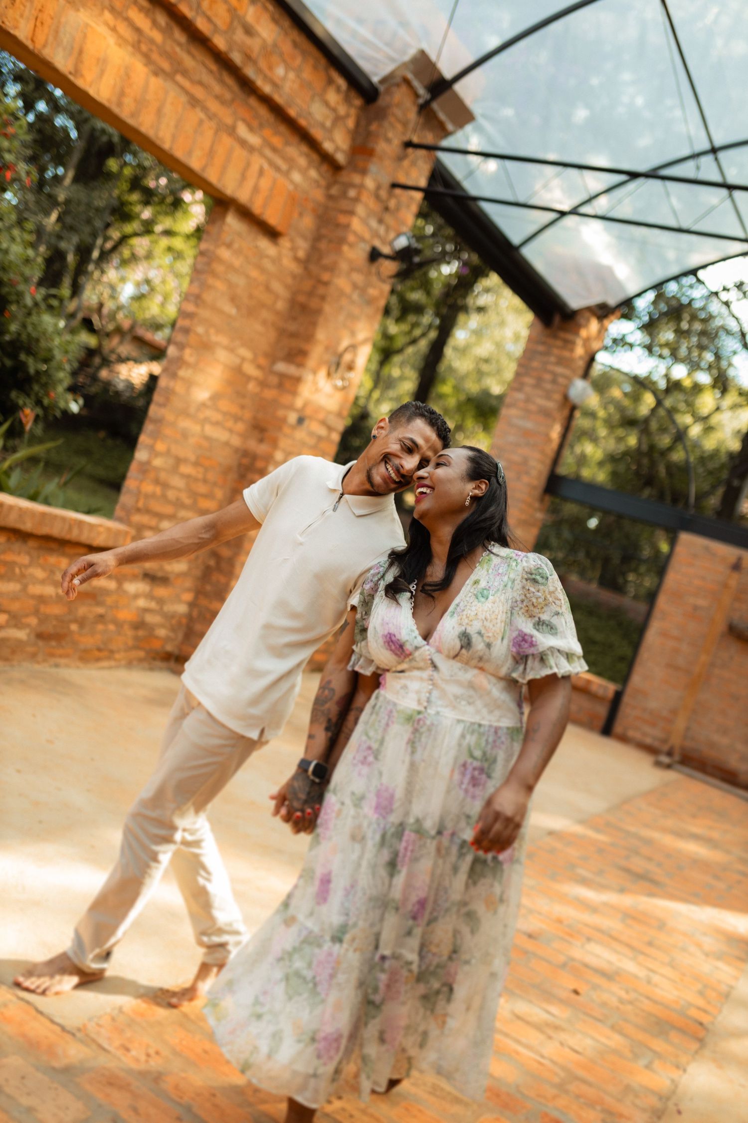 Joyful couple dancing and laughing together under a glass canopy outdoors.