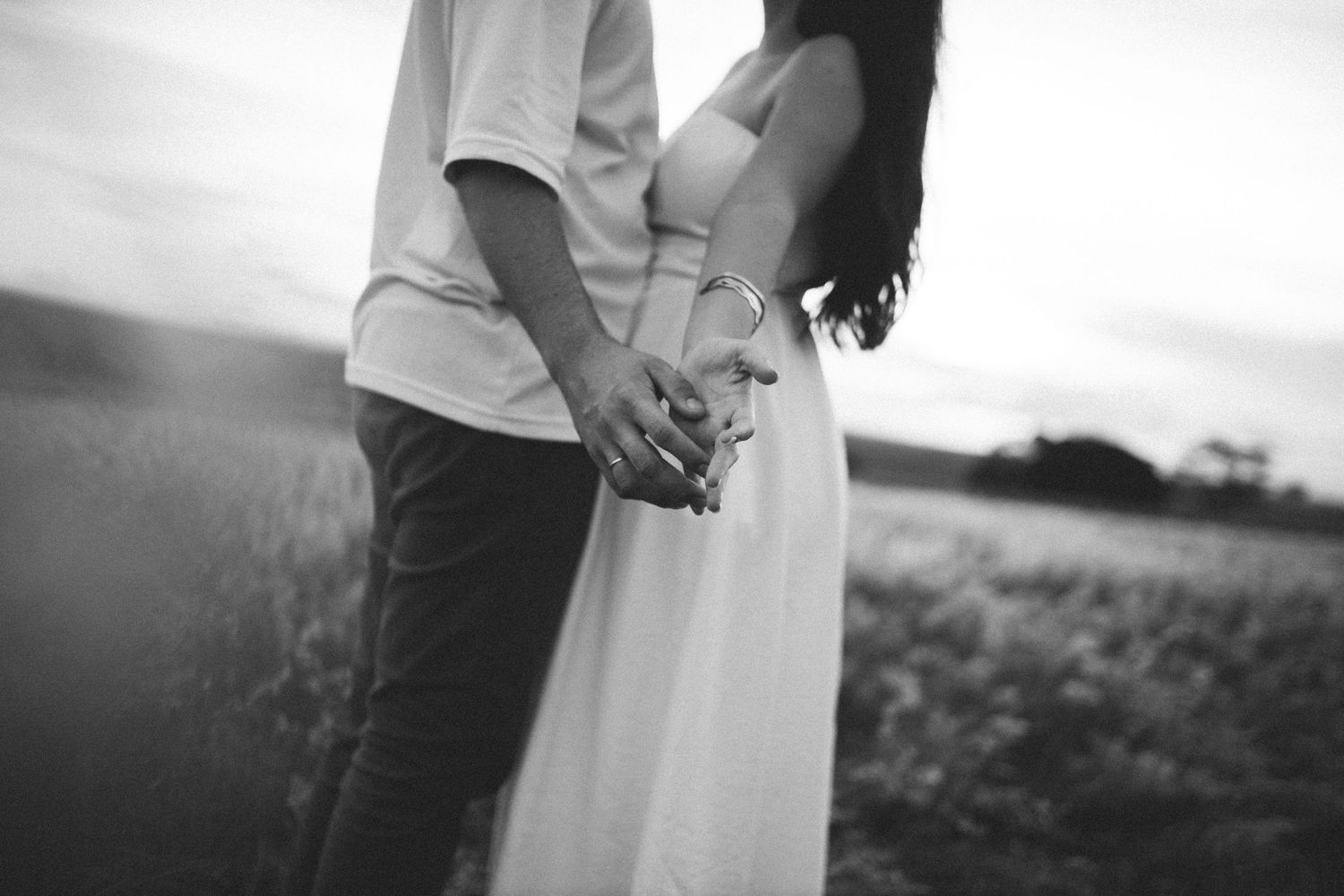 Black and white photo of couple holding hands in a field, woman wearing a flowing white dress.