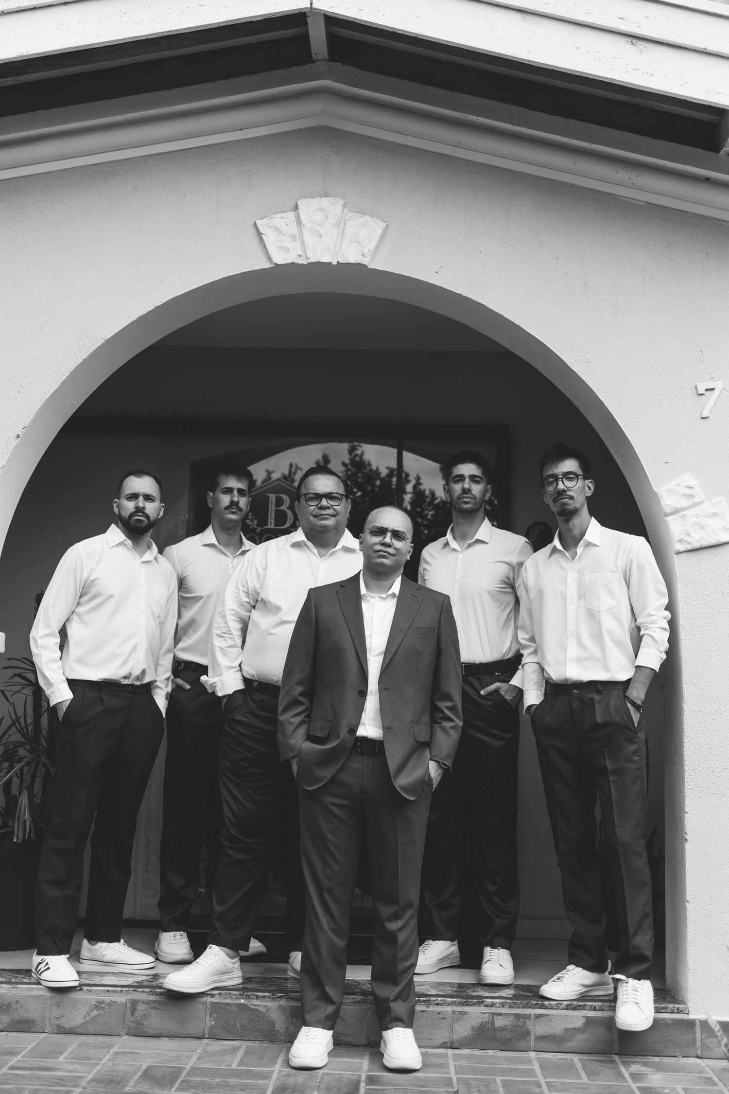 Black and white photo of groom and groomsmen posing under an arched doorway before wedding.