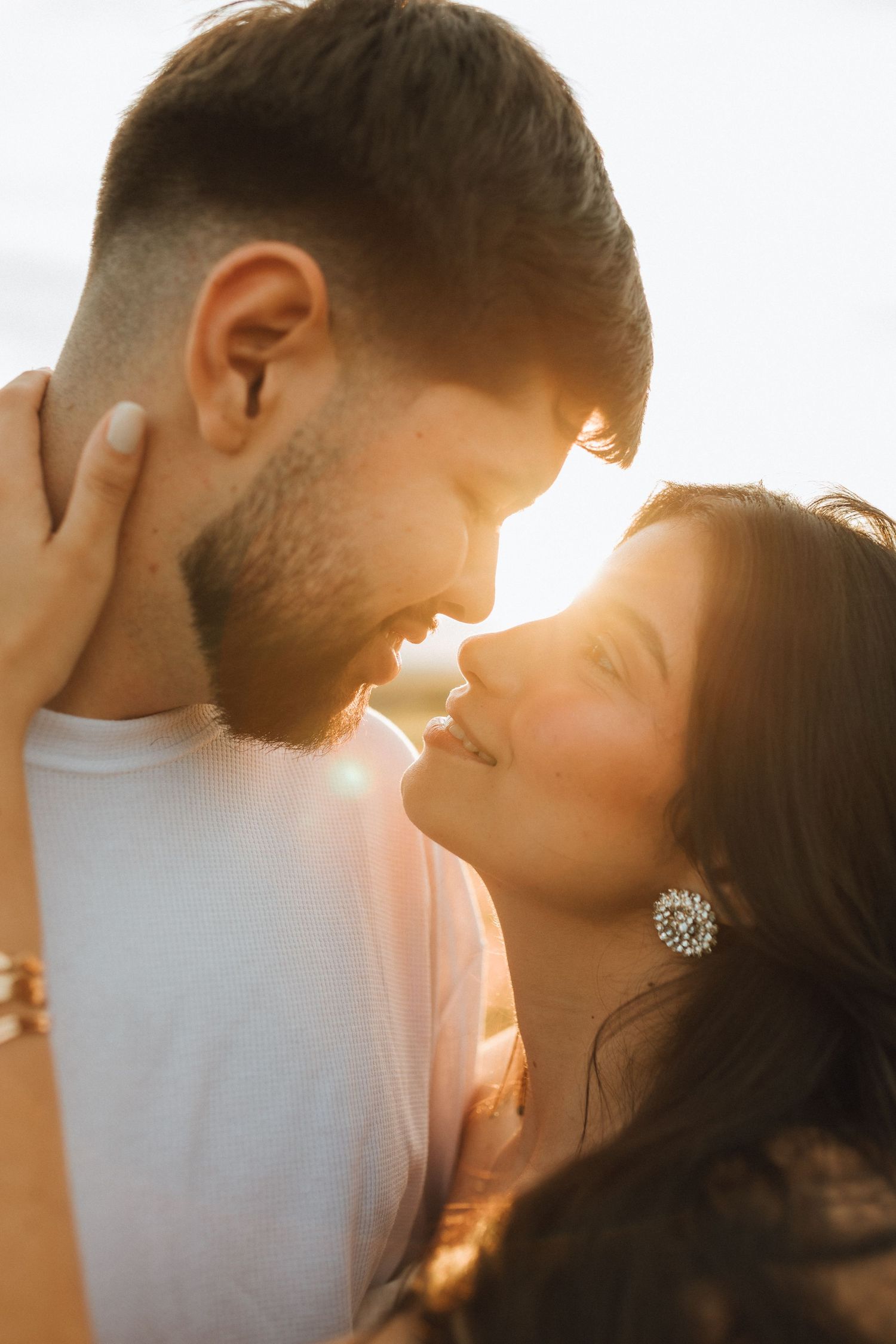 A couple shares a romantic golden hour moment, smiling and about to kiss, bathed in warm sunset backlight.