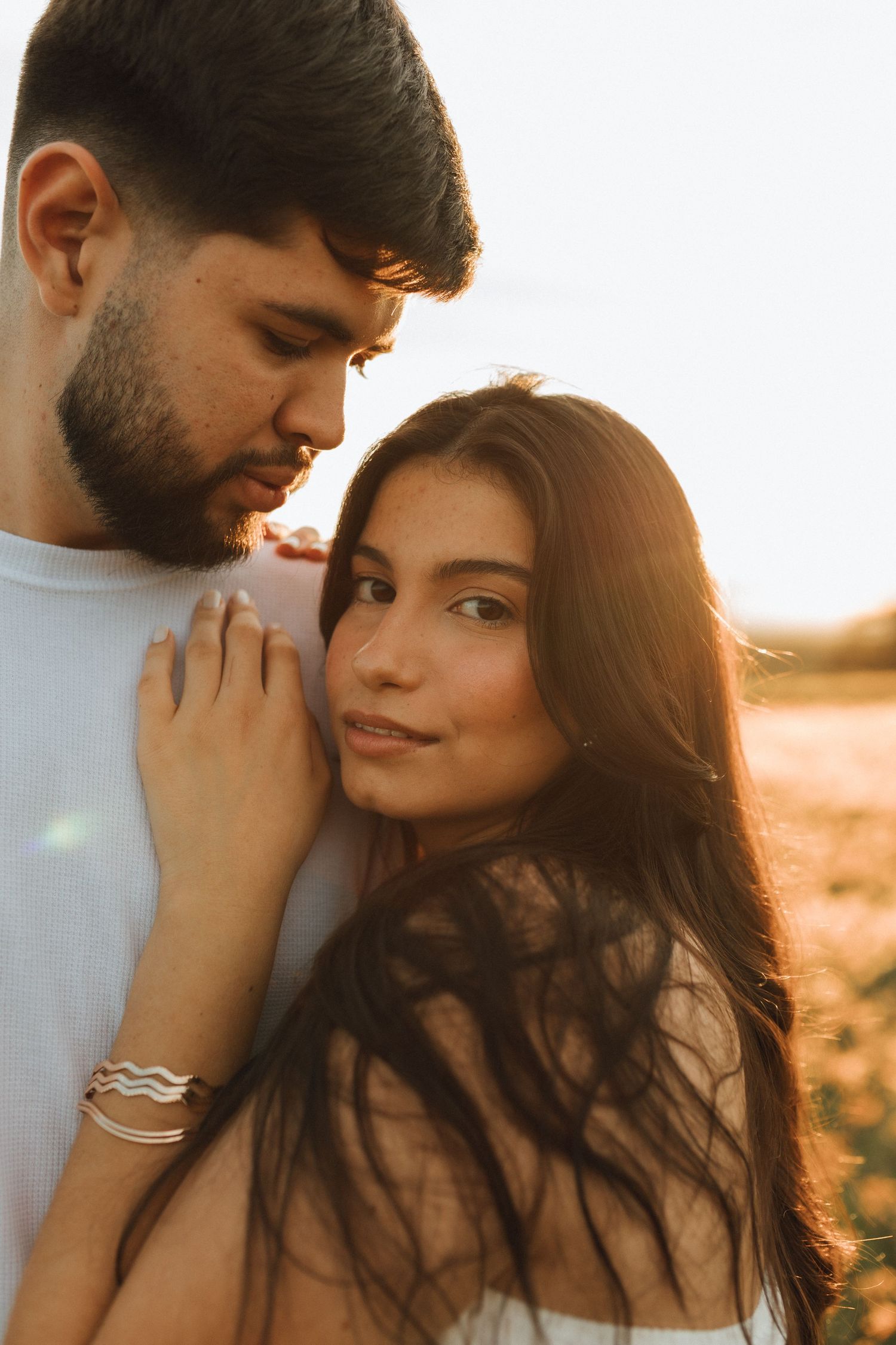 Intimate couple portrait at sunset, woman leaning against mans chest in a glowing field.