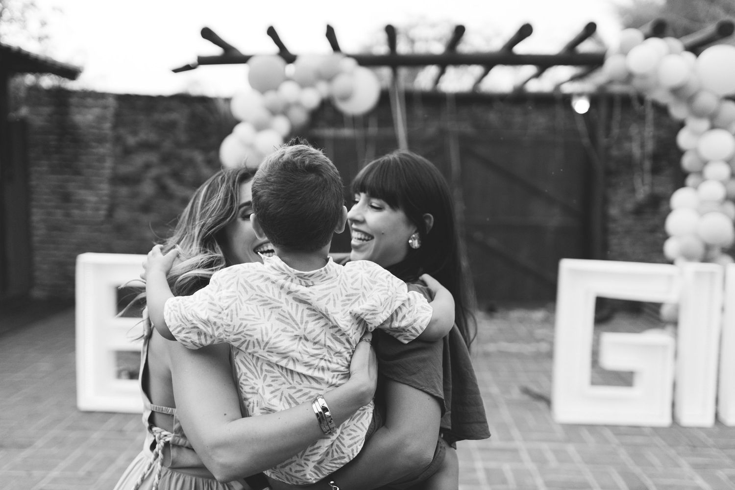 Black and white photo of three people sharing a warm group hug at a gender reveal celebration.