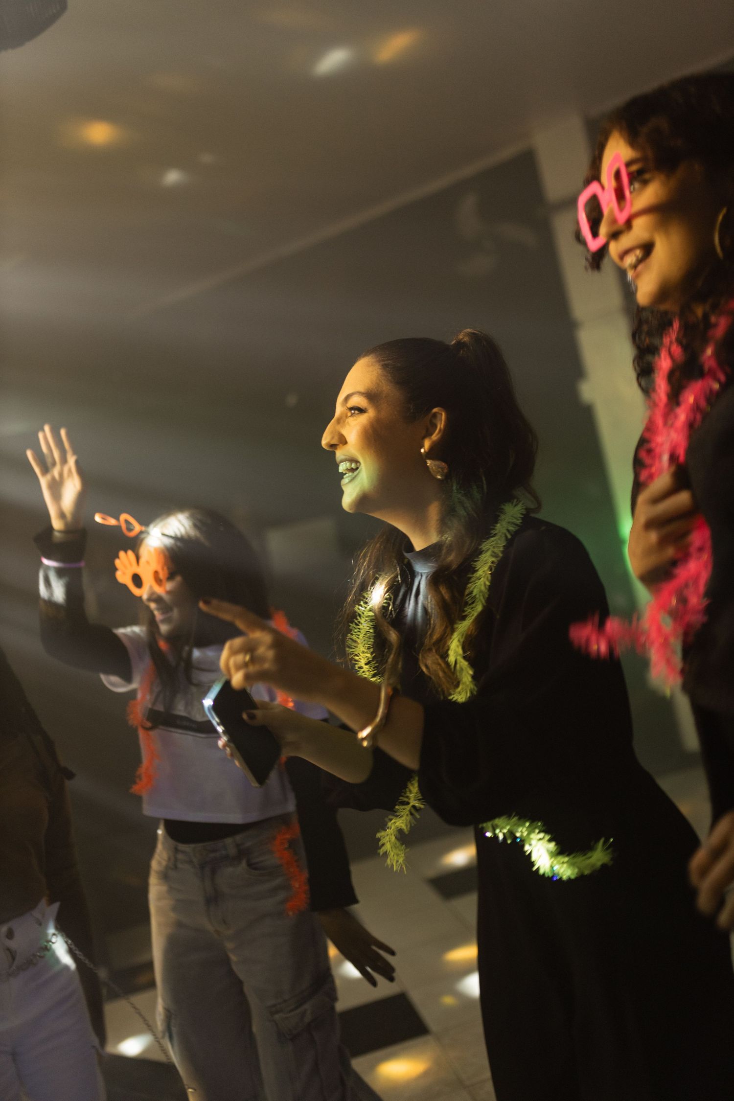 Group of women dancing and celebrating at a birthday party with colorful disco lights overhead.