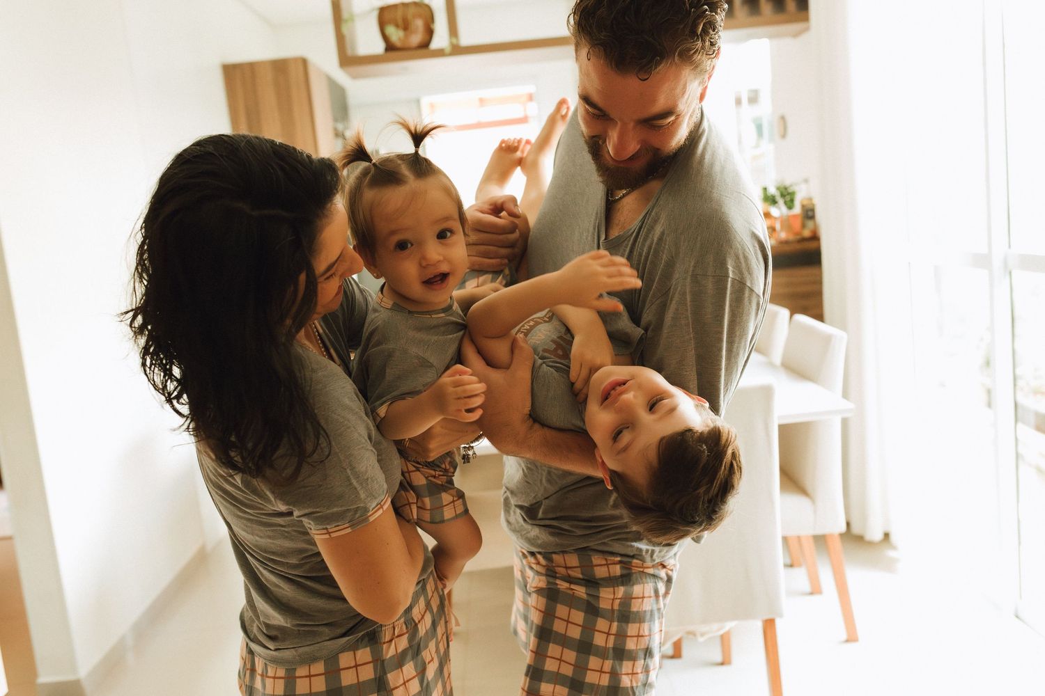Happy family in matching pajamas playing with two young children in a bright, modern home.