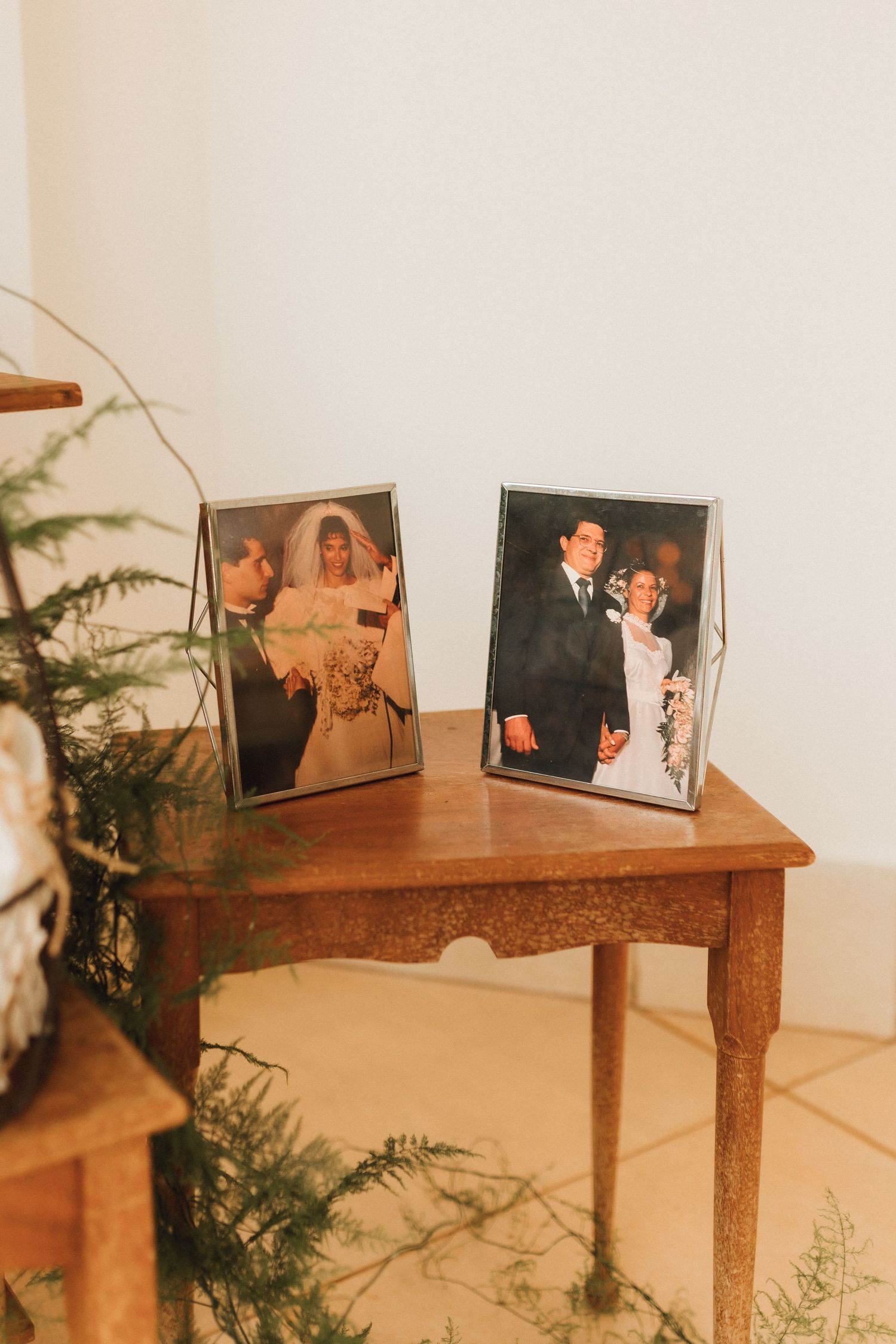Two framed vintage wedding photos displayed on a wooden table with greenery decor.
