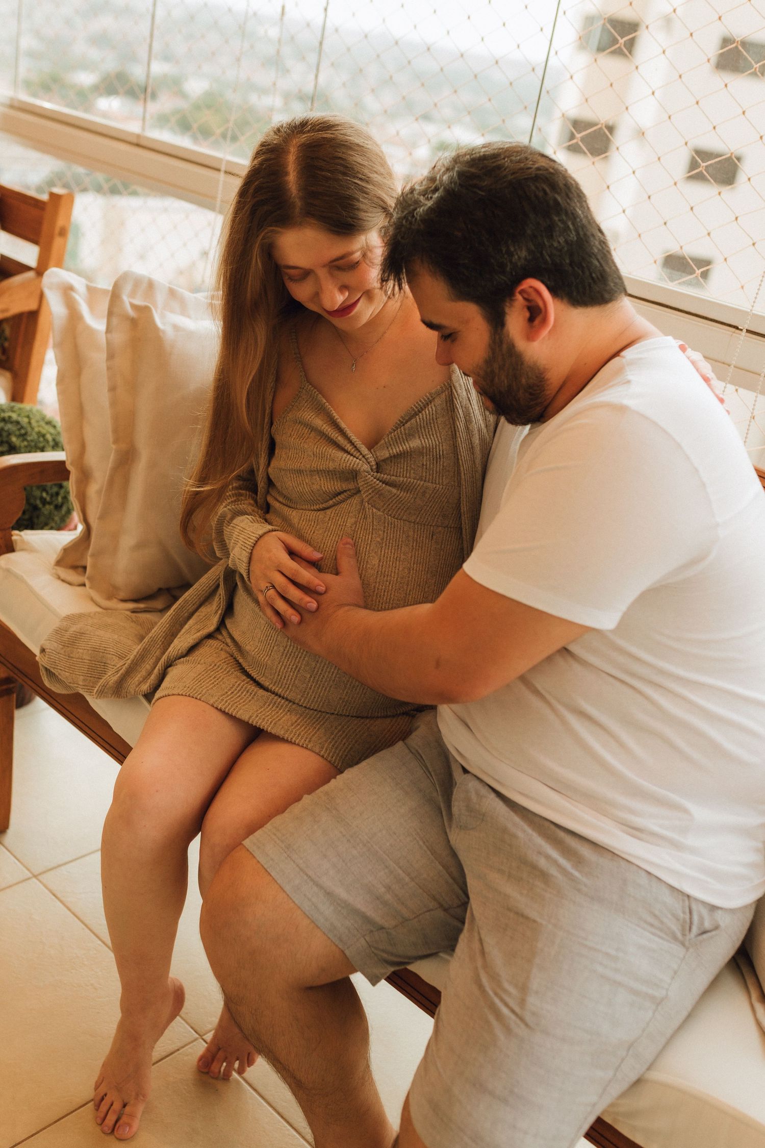 Loving couple on balcony, man tenderly touching pregnant woman's belly while she smiles warmly at him.