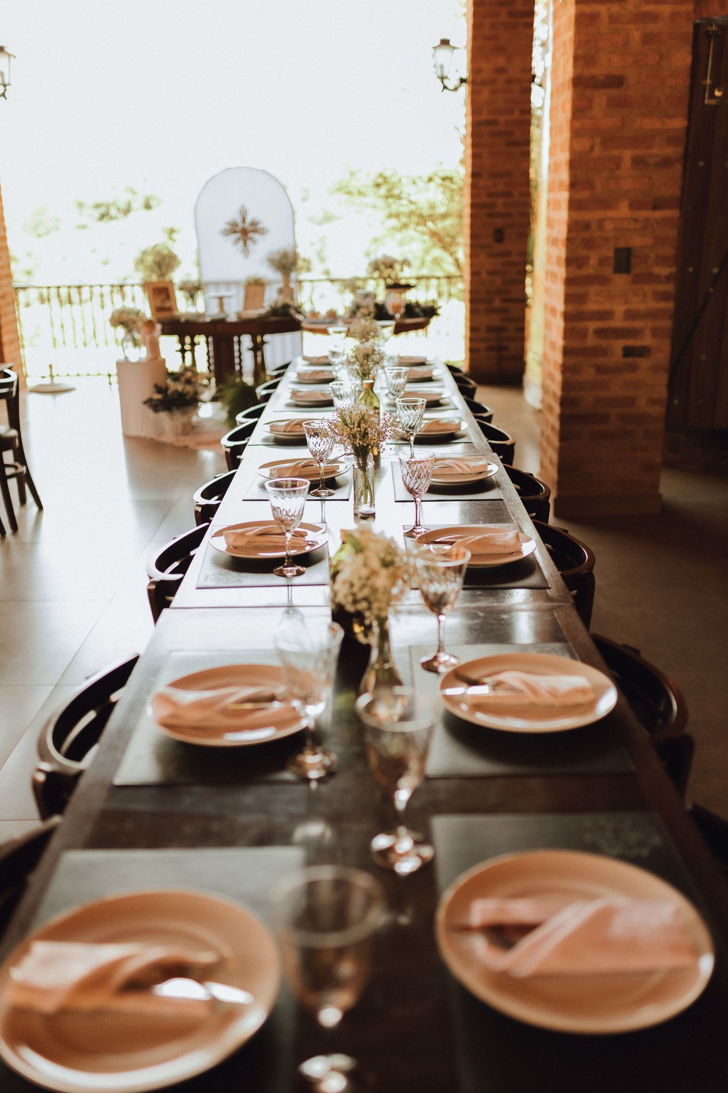 Elegant long dining table set with pink napkins, glassware, and floral centerpieces in a rustic venue.