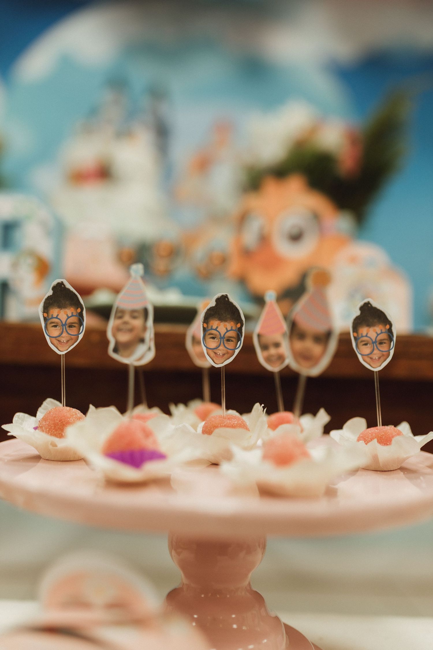 Pink cake stand with cute face toppers on mini desserts at a kids birthday party.