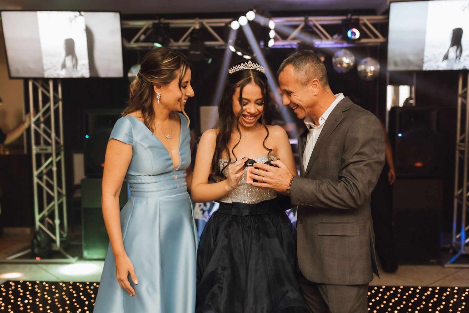 Parents present a gift to their daughter in tiara and black dress at her quinceañera celebration.