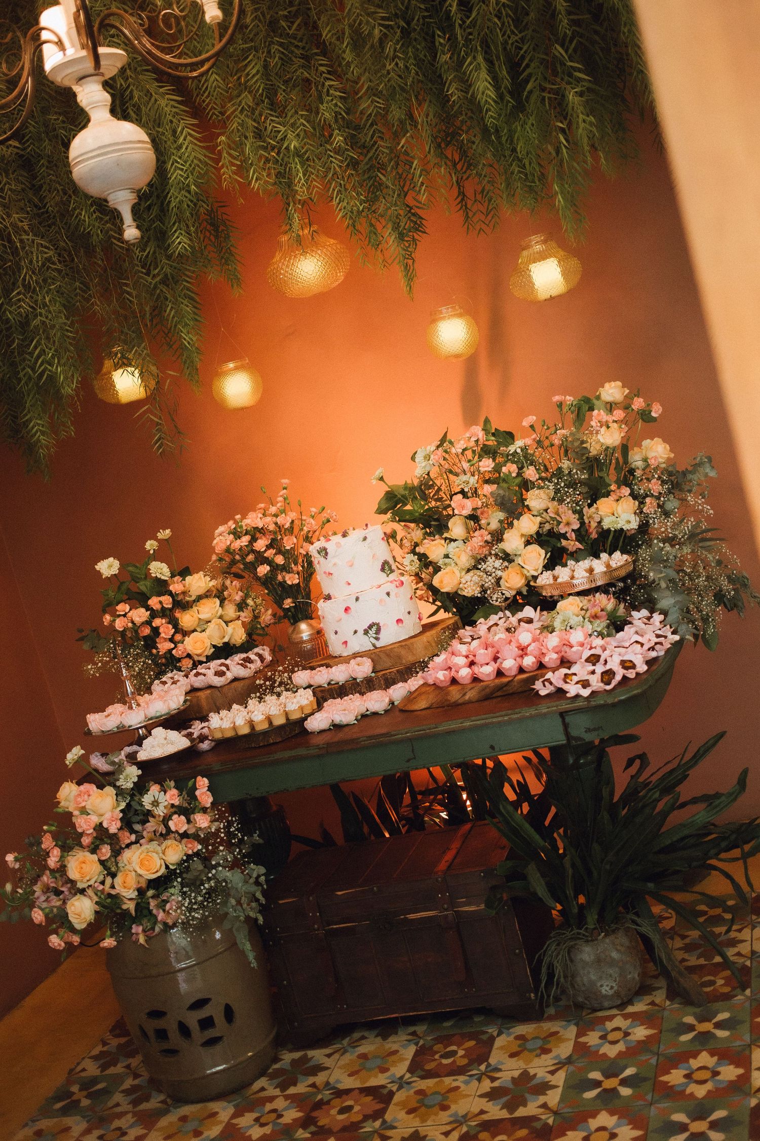 Rustic wedding dessert table with floral arrangements, wedding cake, and string lights.