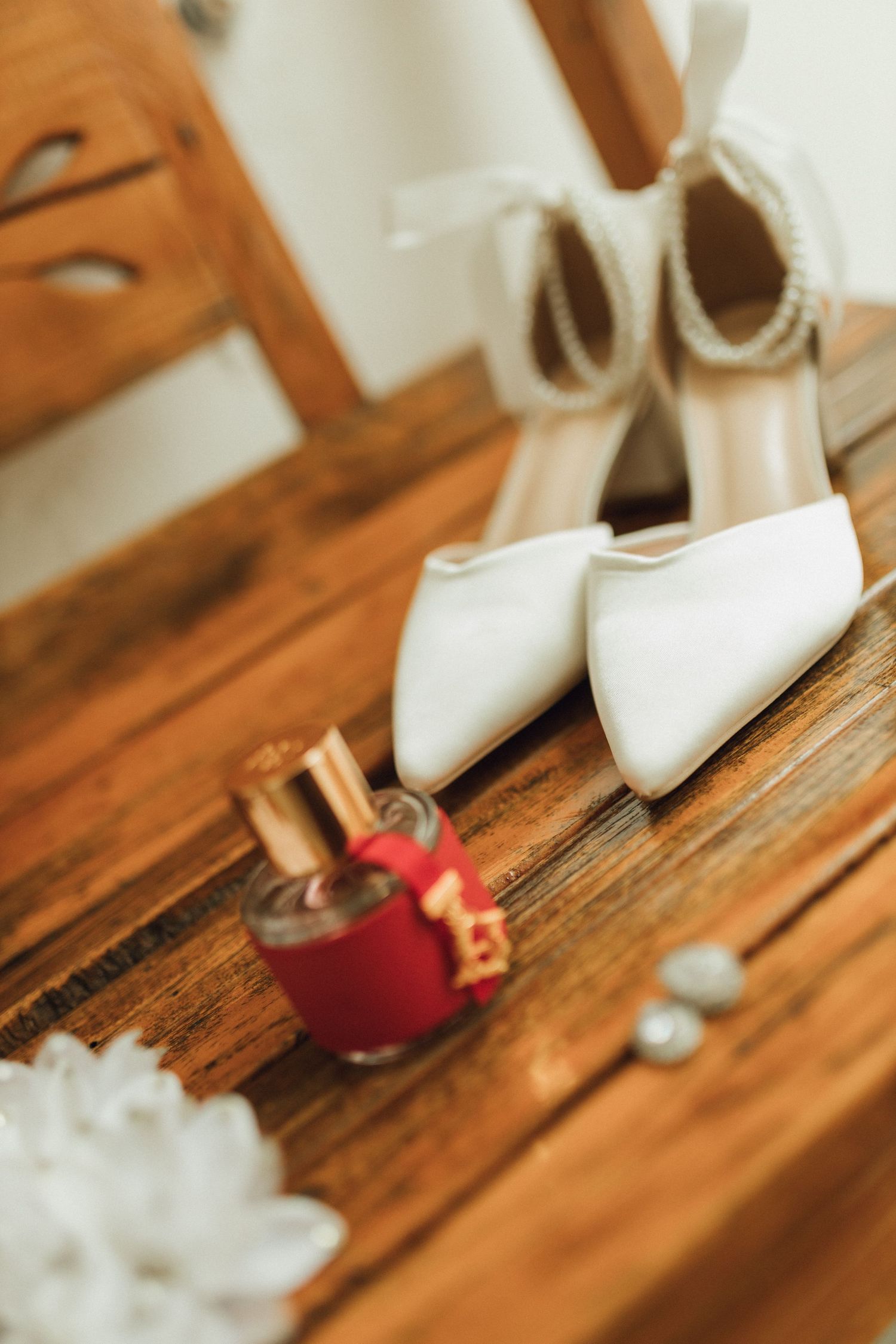 White bridal heels with ankle ties beside red nail polish bottle on wooden dresser surface.
