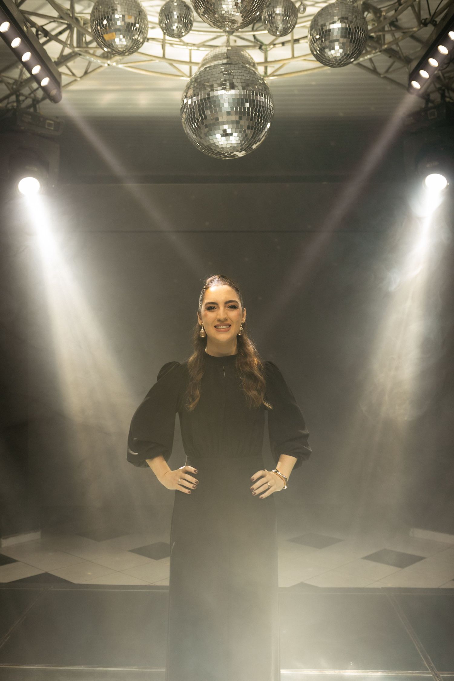 Woman in black dress posing under disco ball with dramatic stage lighting and smoke effects at a birthday party.