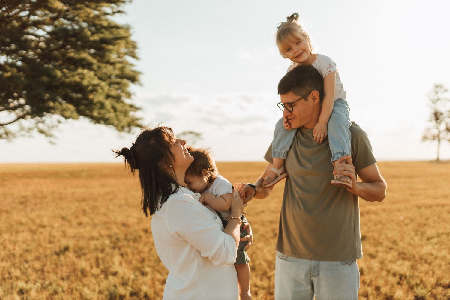 Happy family with two young children enjoys golden hour in open wheat field.