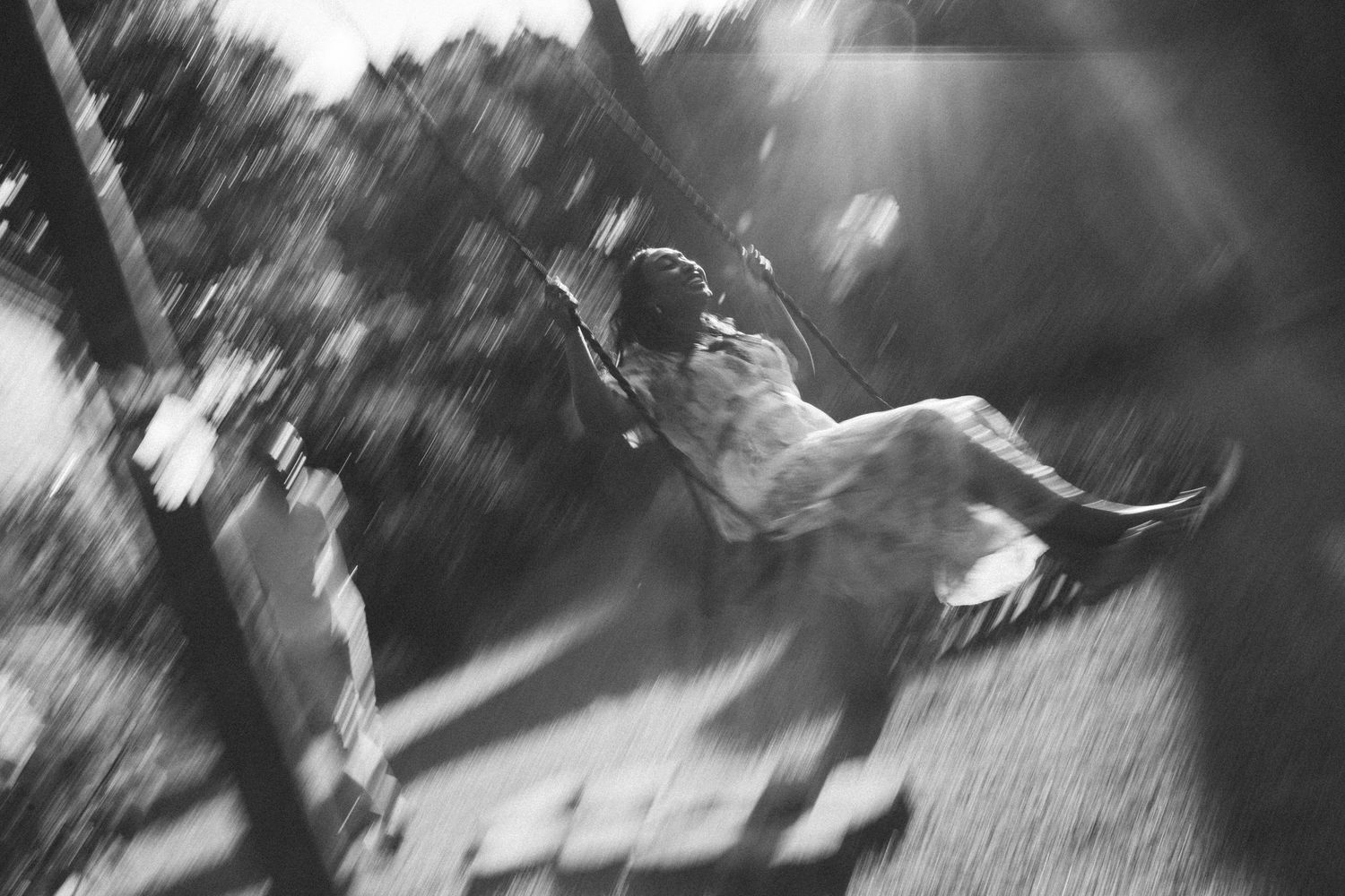 Black and white photo of a child joyfully swinging on a playground swing, motion blur capturing the carefree movement.