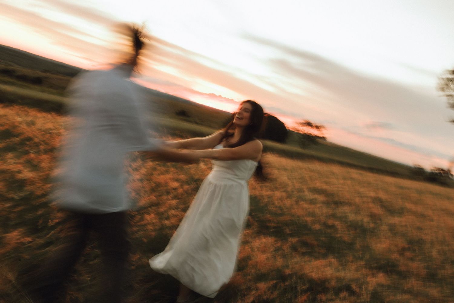 Motion blur photo of couple spinning together in a golden field at dramatic sunset.