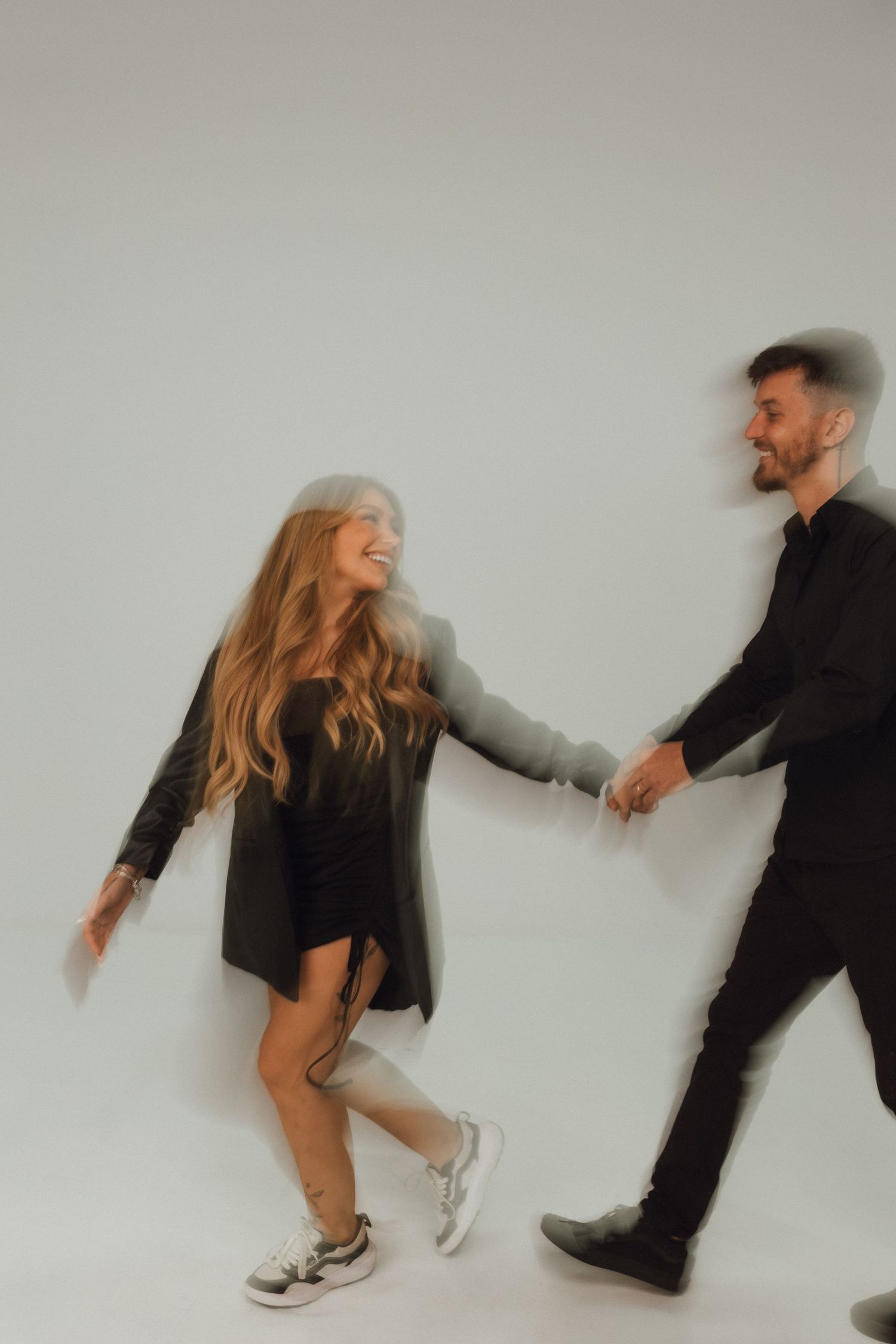 A joyful couple holding hands and dancing together in a studio, captured with a motion blur effect.