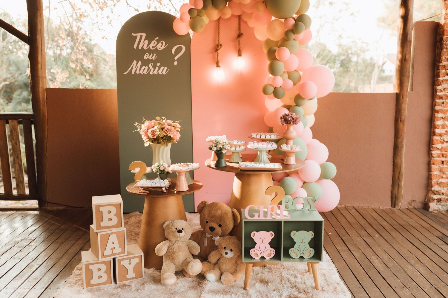 Gender reveal party decor with pink and green balloons, teddy bears, baby blocks, and a chalkboard sign reading Theo ou Maria.