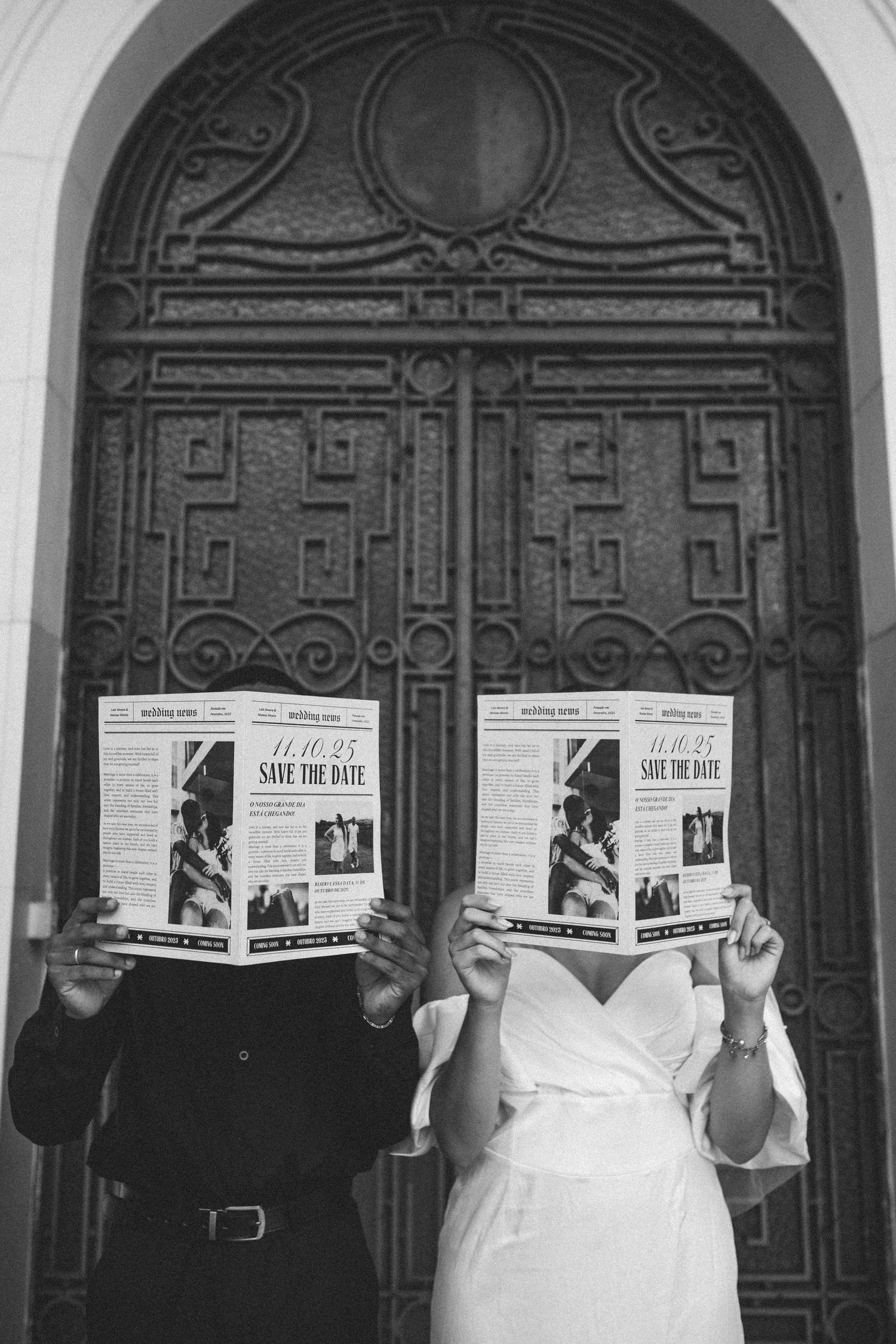 Couple holding Save the Date newspapers in front of ornate door, black and white wedding photo.