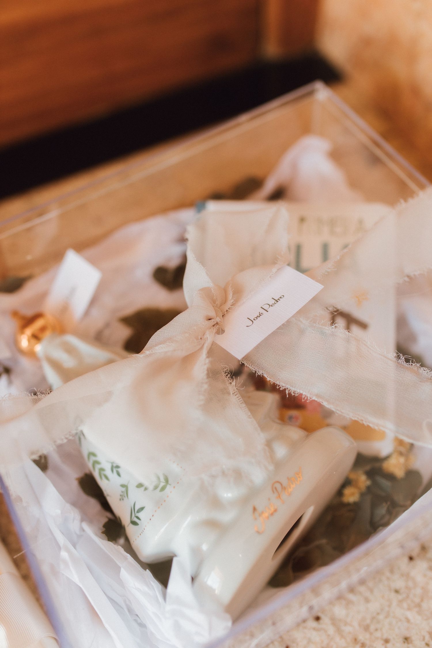 Elegant sheer organza gift bags with handwritten tags displayed in a clear box for a wedding favor arrangement.