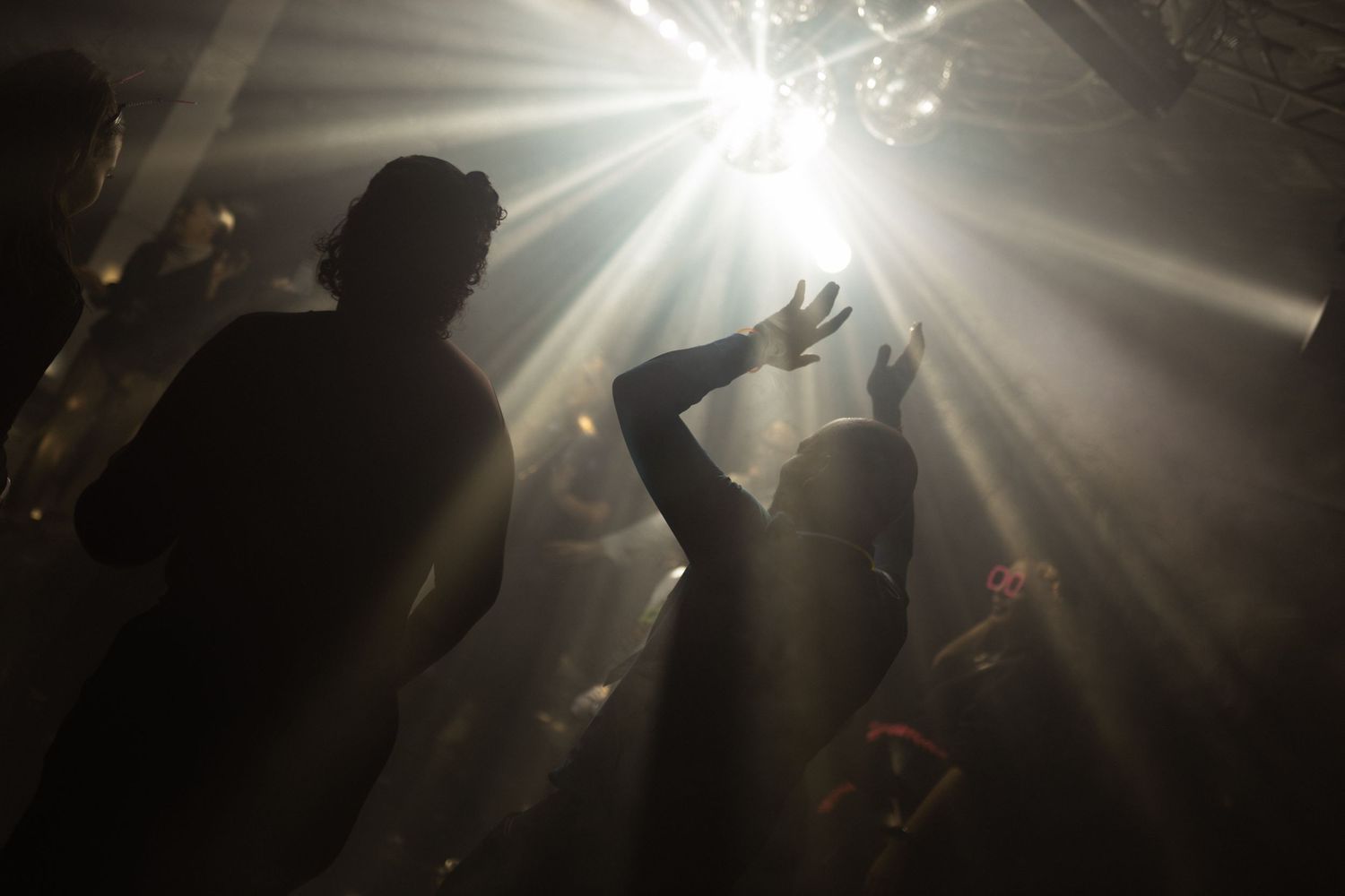 Silhouettes of people dancing in a nightclub with dramatic light beams shining from above.