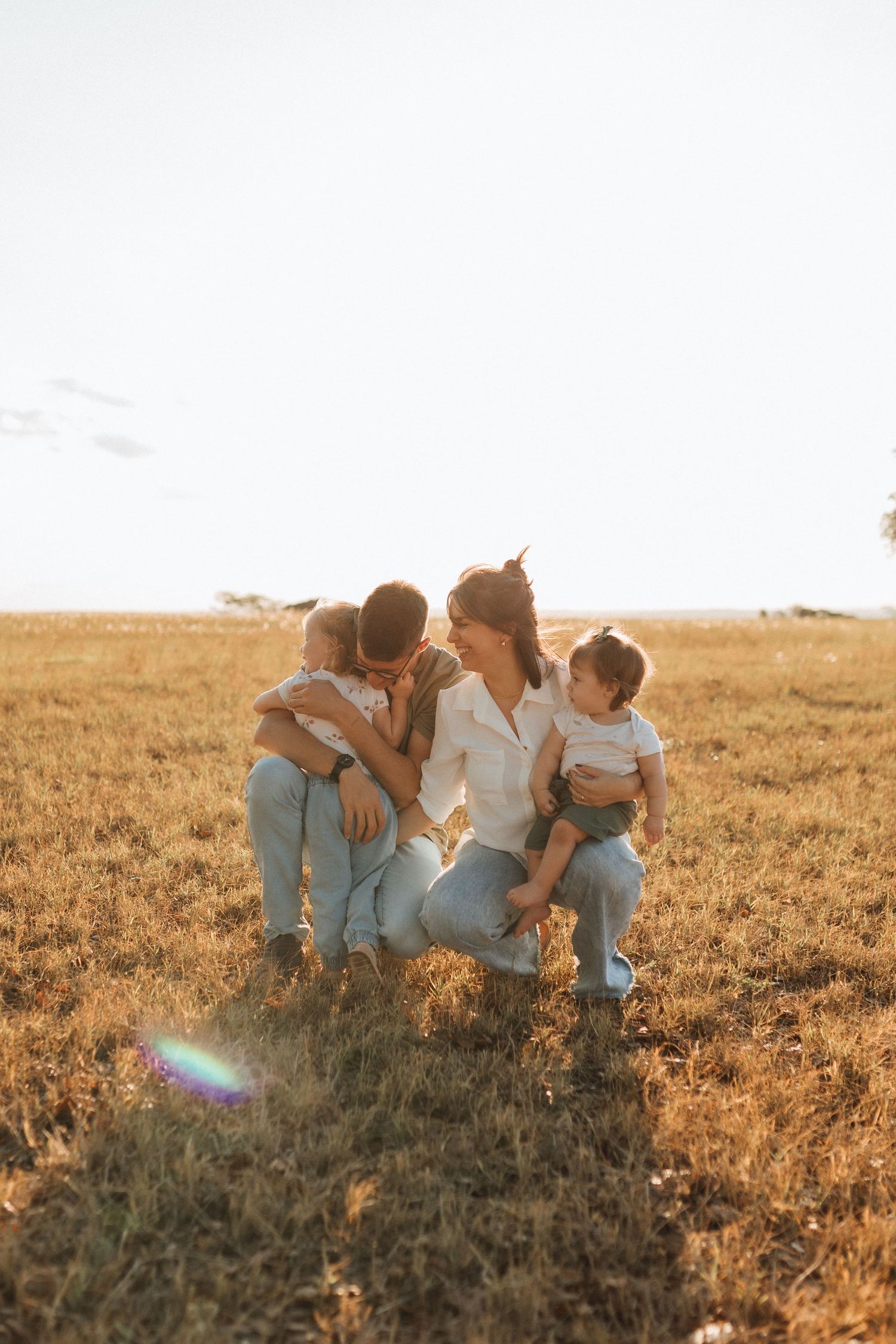 Family of four embracing in a sunlit golden field during a warm sunset.