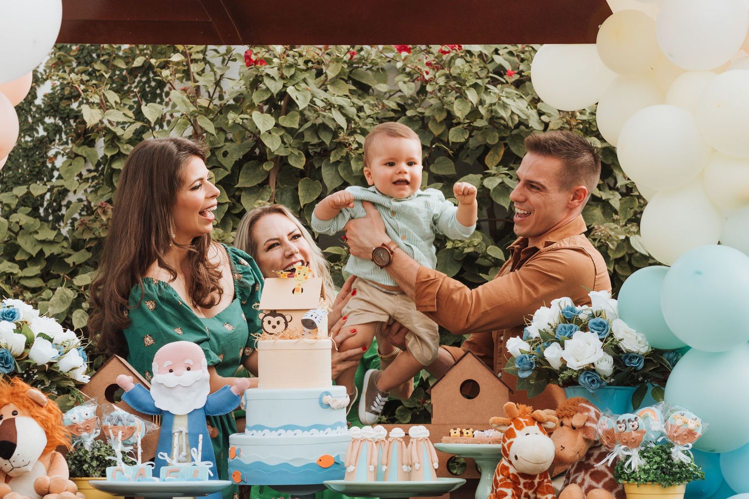 Family celebrating baby's first birthday party with cake, balloons, and decorations outdoors.