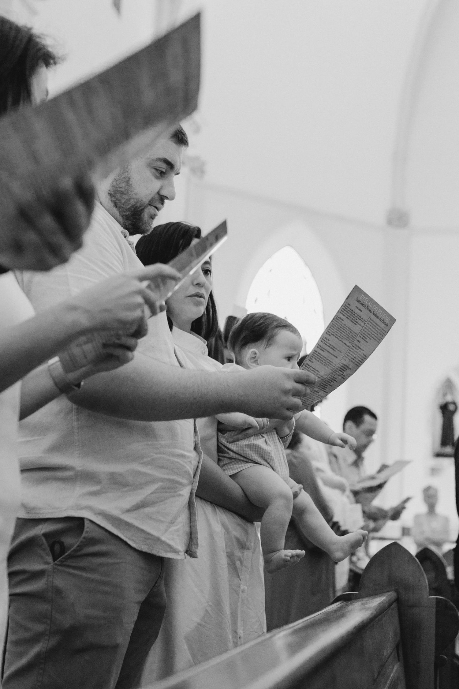 Black and white photo of a family standing in church pews, holding programs and singing during a religious service.