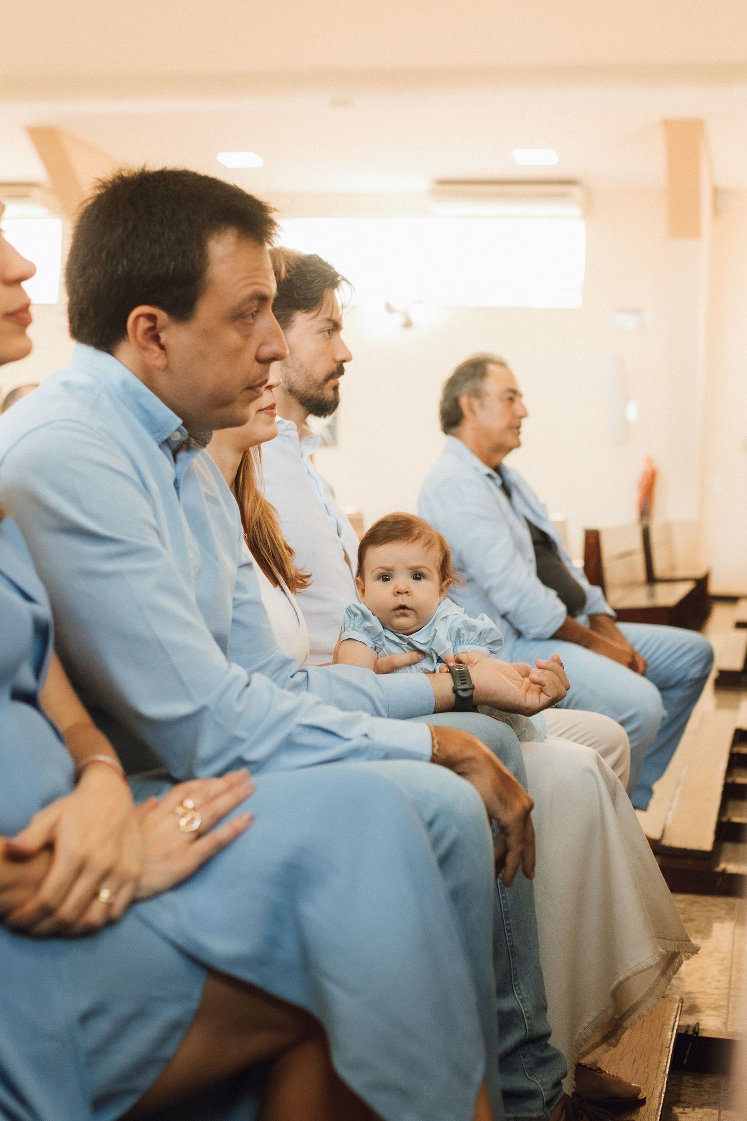 Family dressed in light blue attire seated in church pews during a baptism ceremony with a baby.