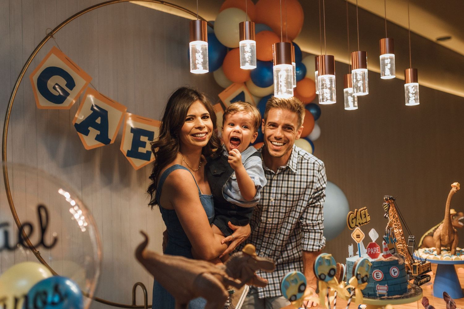 Family celebrating baby's first birthday party with colorful decorations and hanging lights.