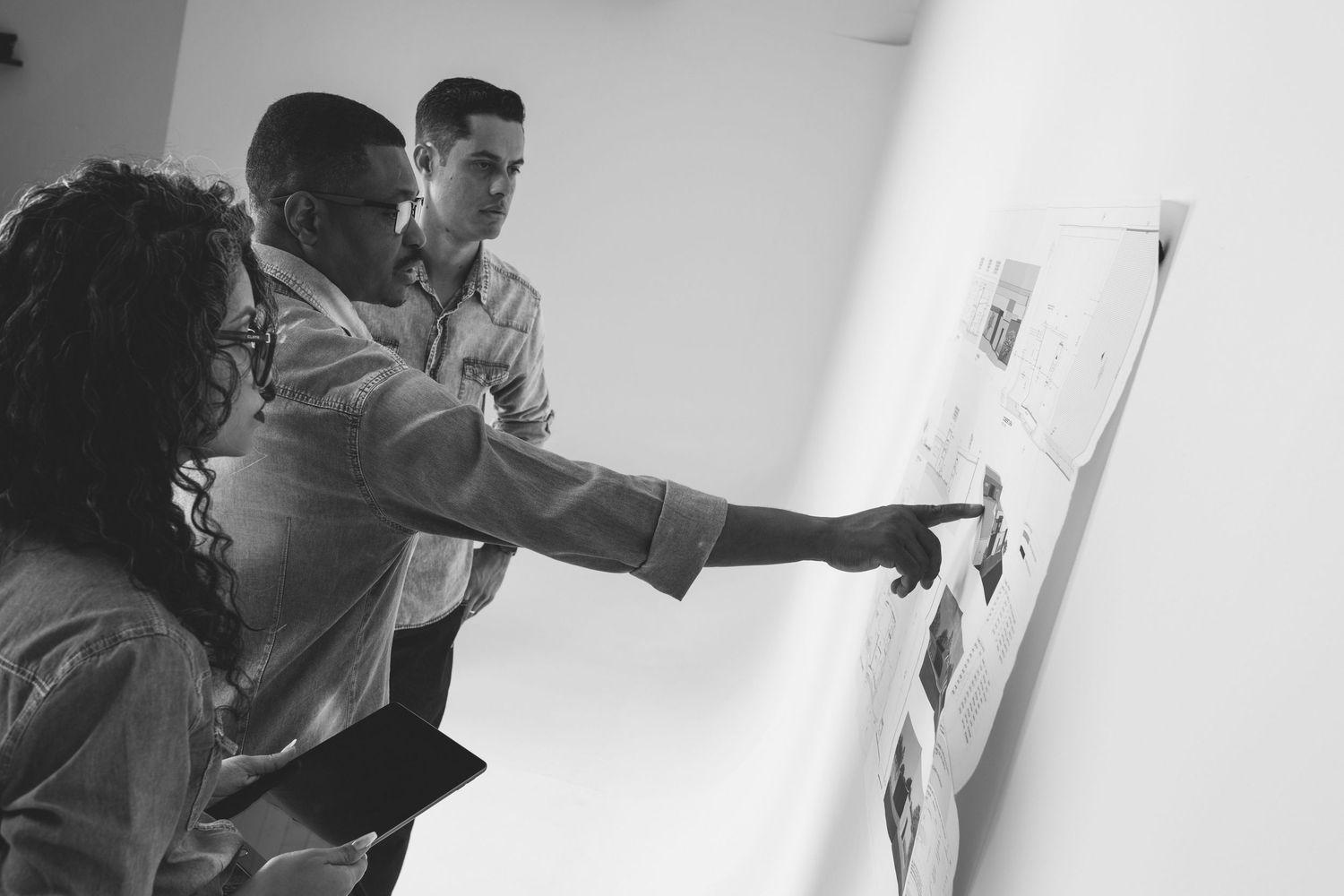 Three colleagues reviewing documents on whiteboard in black and white photo.
