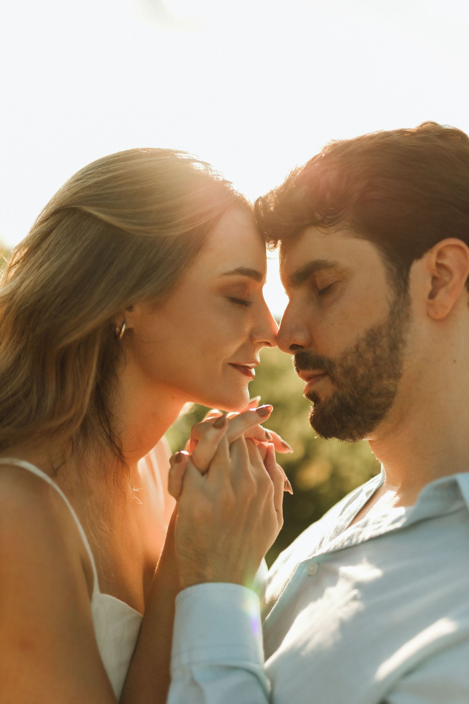 Couple touching foreheads tenderly holding hands in warm golden sunset backlight outdoors.