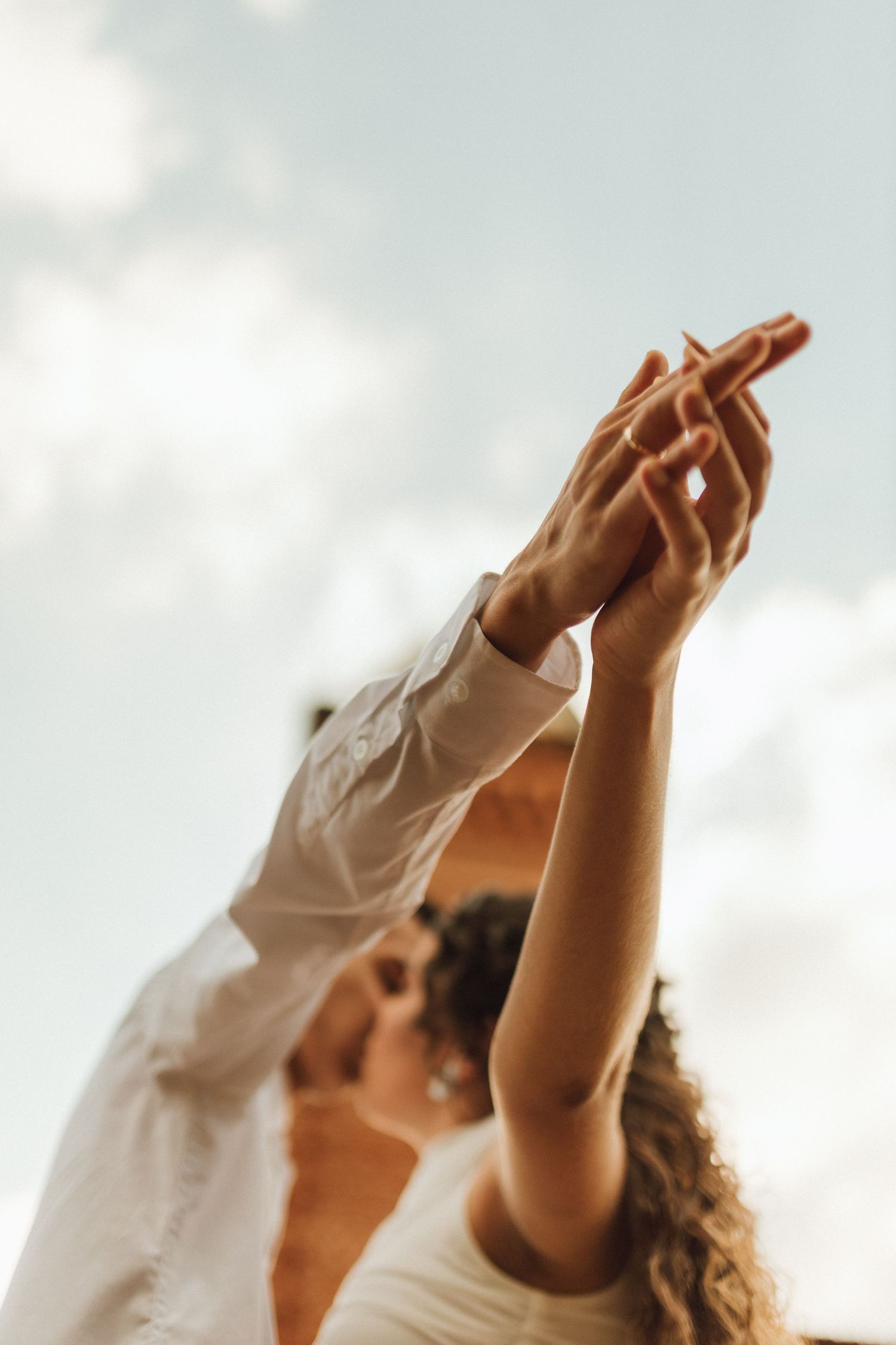 Close-up of a couple holding hands raised toward a cloudy sky, symbolizing love and togetherness.