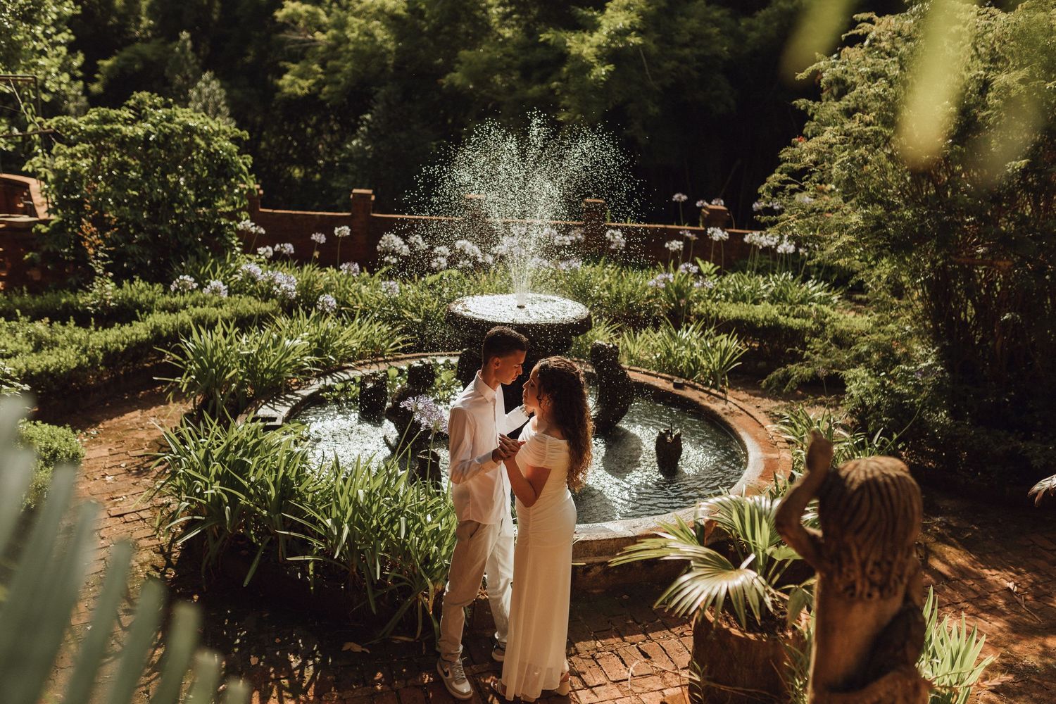Couple sharing a romantic moment by a garden fountain surrounded by lush greenery on their wedding day.