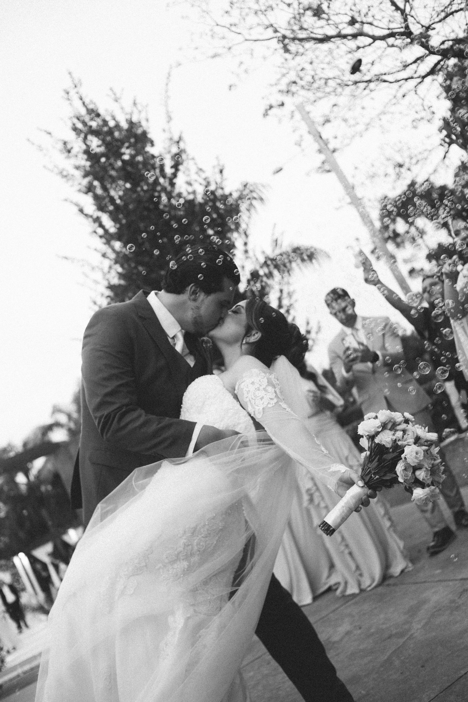 Bride and groom share a passionate kiss surrounded by bubbles at outdoor ceremony.