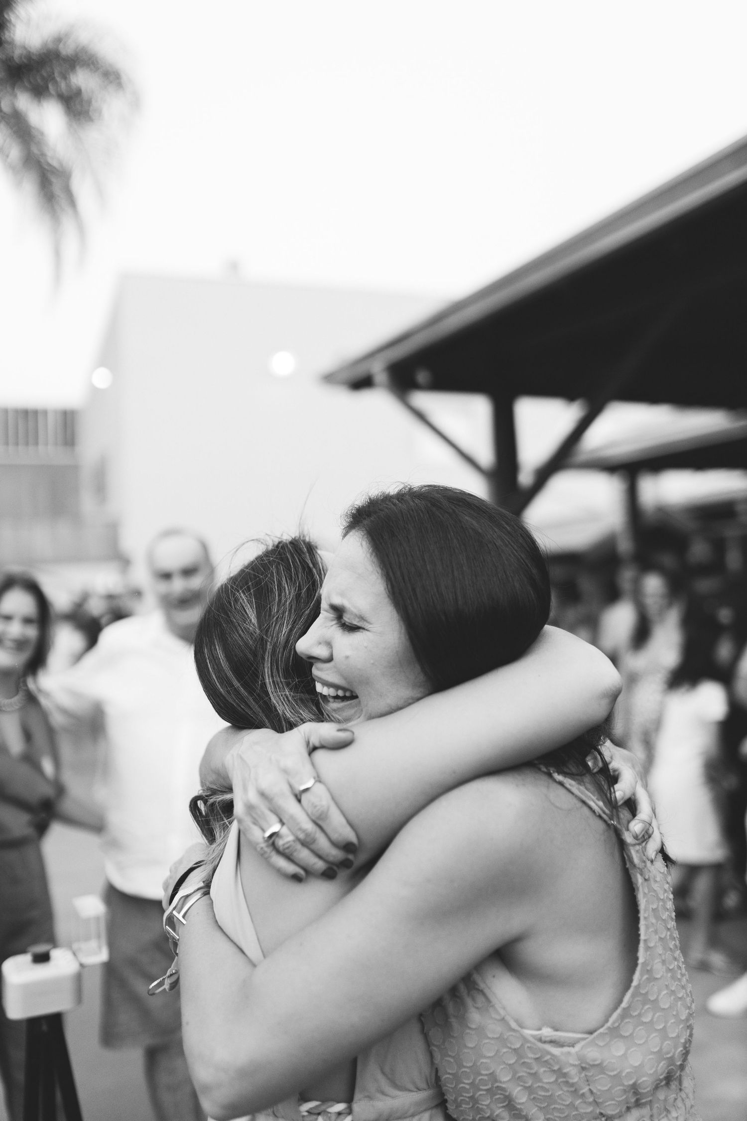 Two women sharing a joyful hug at an outdoor event in black and white photography.