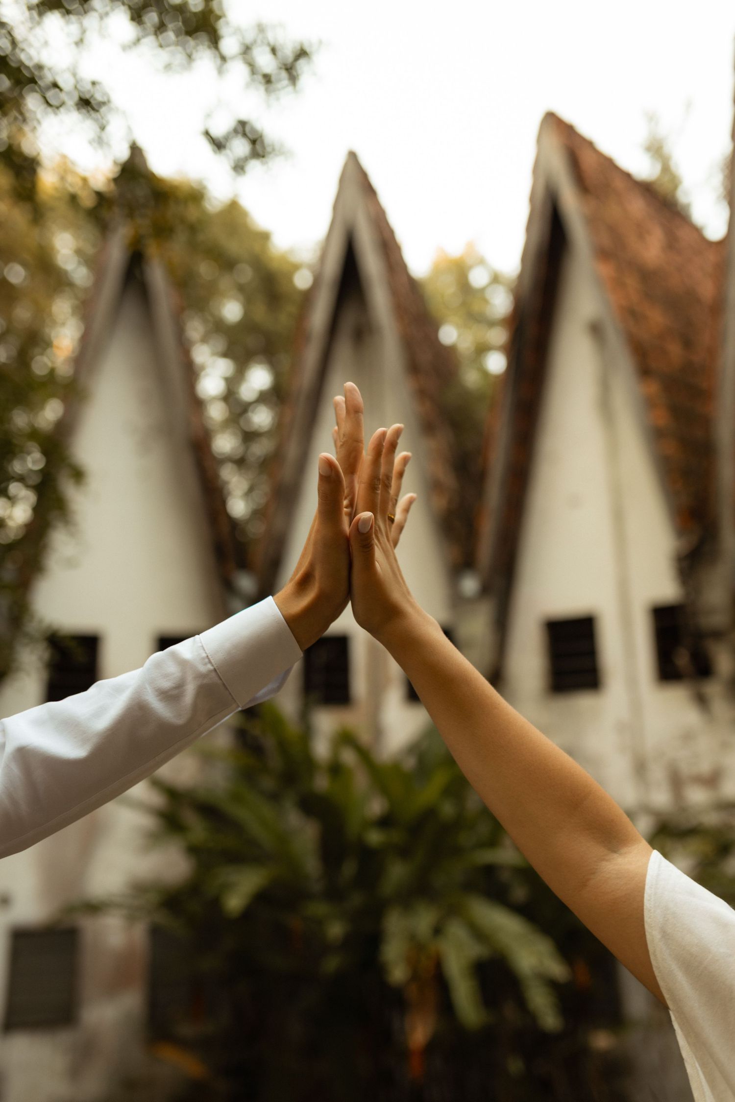 Two people high-fiving in front of a white building with pointed roofs surrounded by lush greenery.