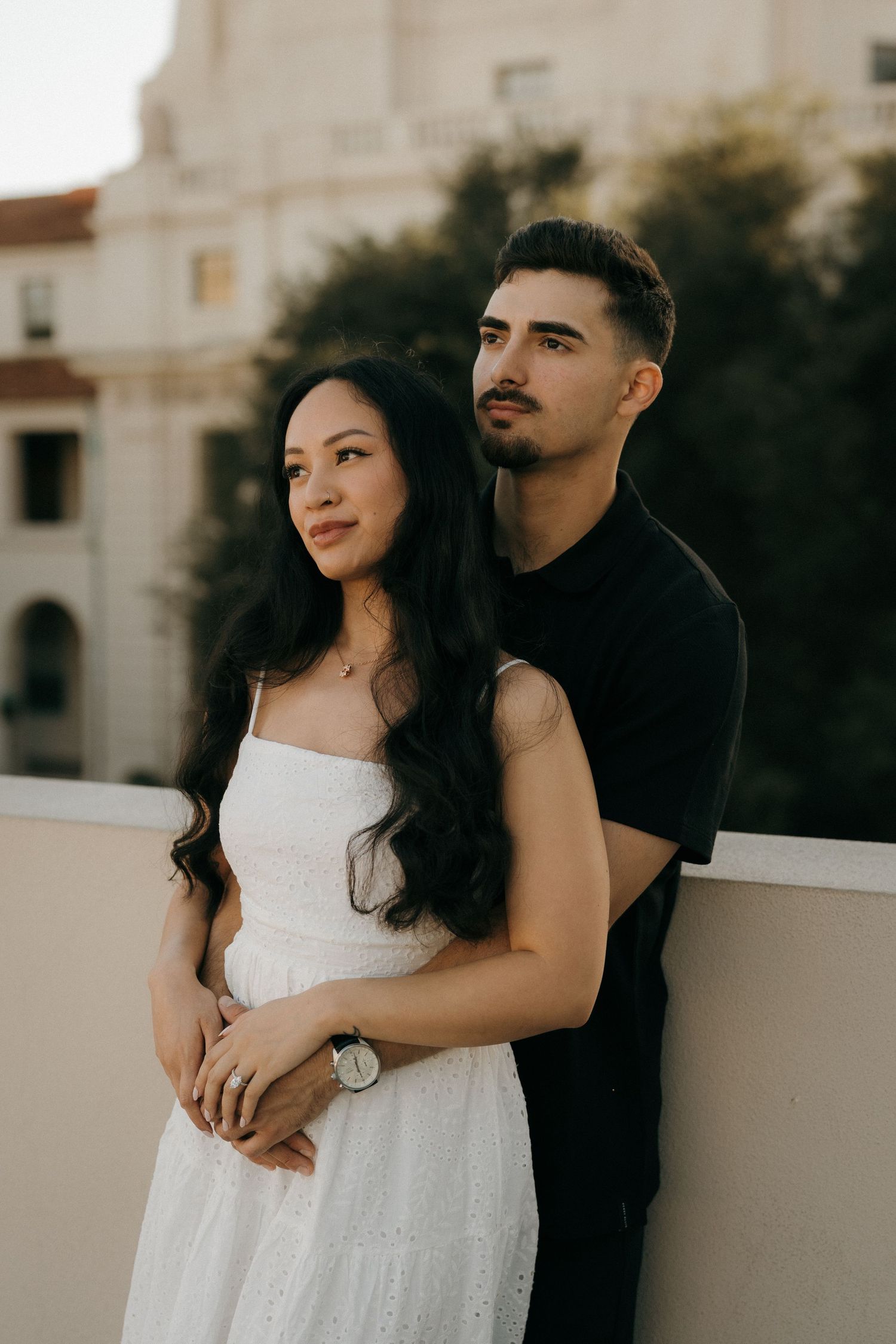 Engaged couple embracing while looking out into the distance at Pasadena City Hall.