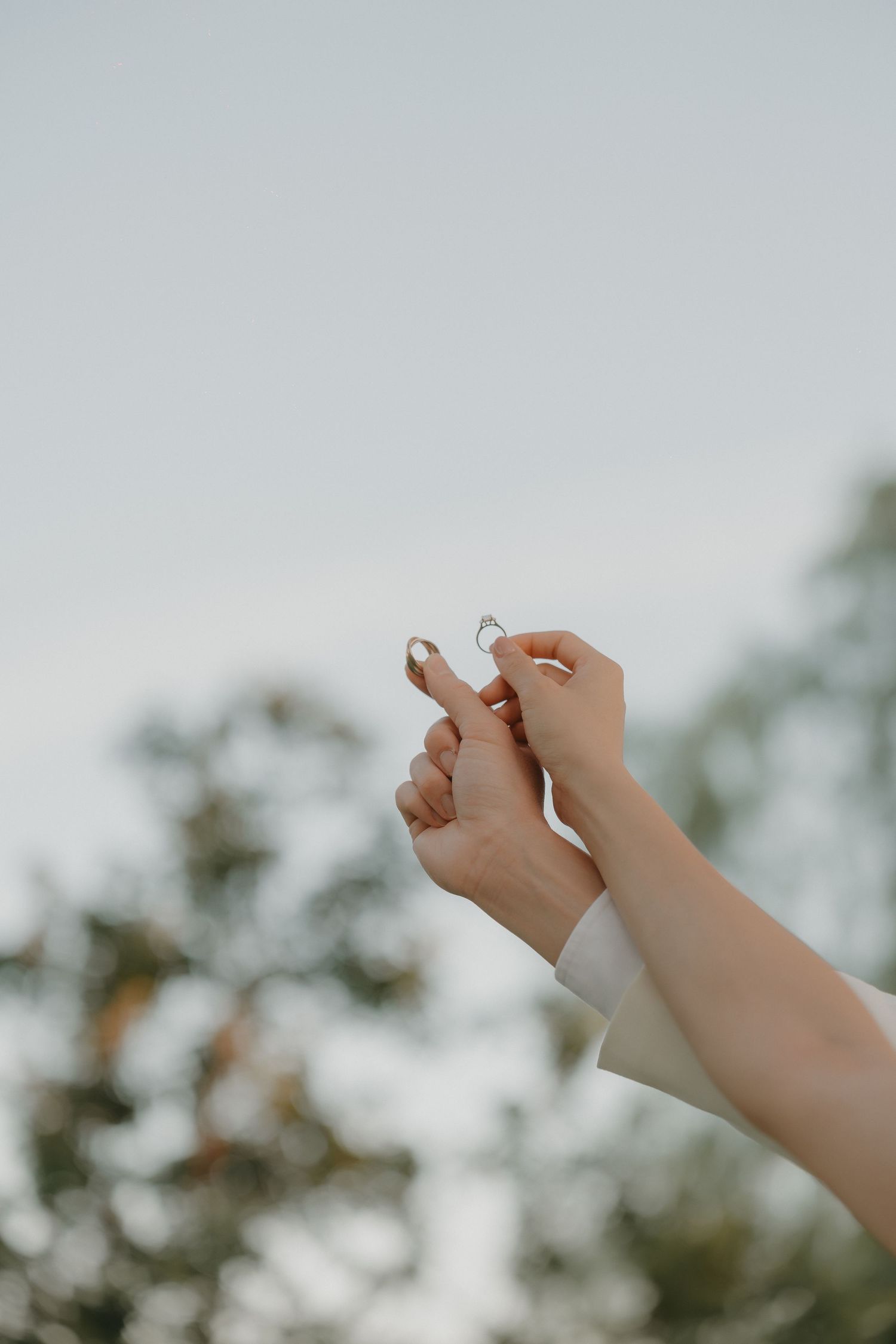 Newlyweds holding their wedding and engagement rings with the sky in the background.