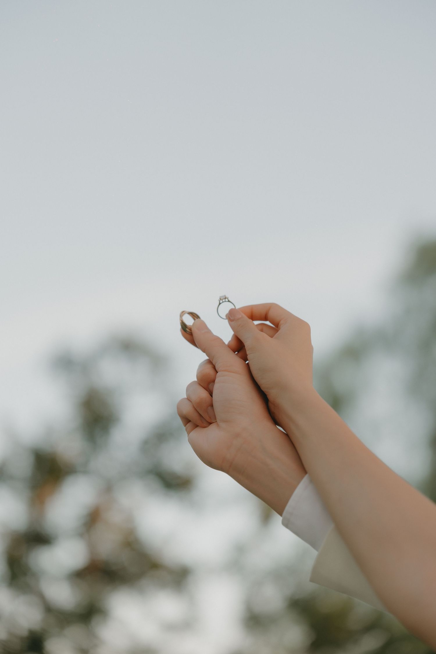 Newlyweds holding their wedding and engagement rings with the sky in the background.