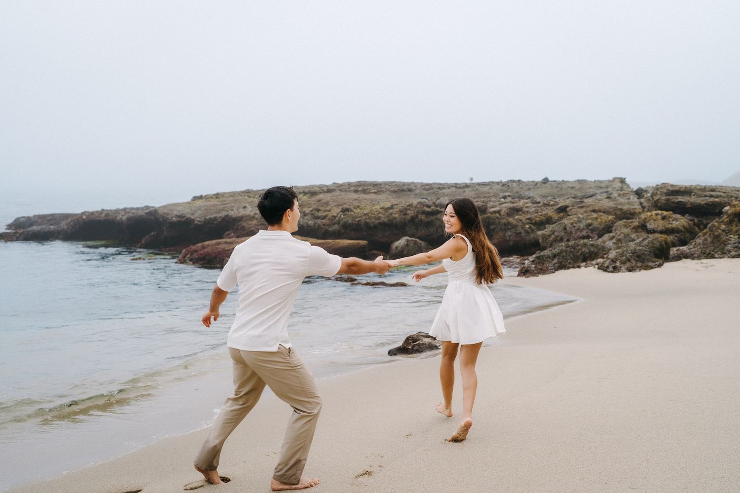 Couple running hand in hand during an engagement photo session in Laguna Beach.