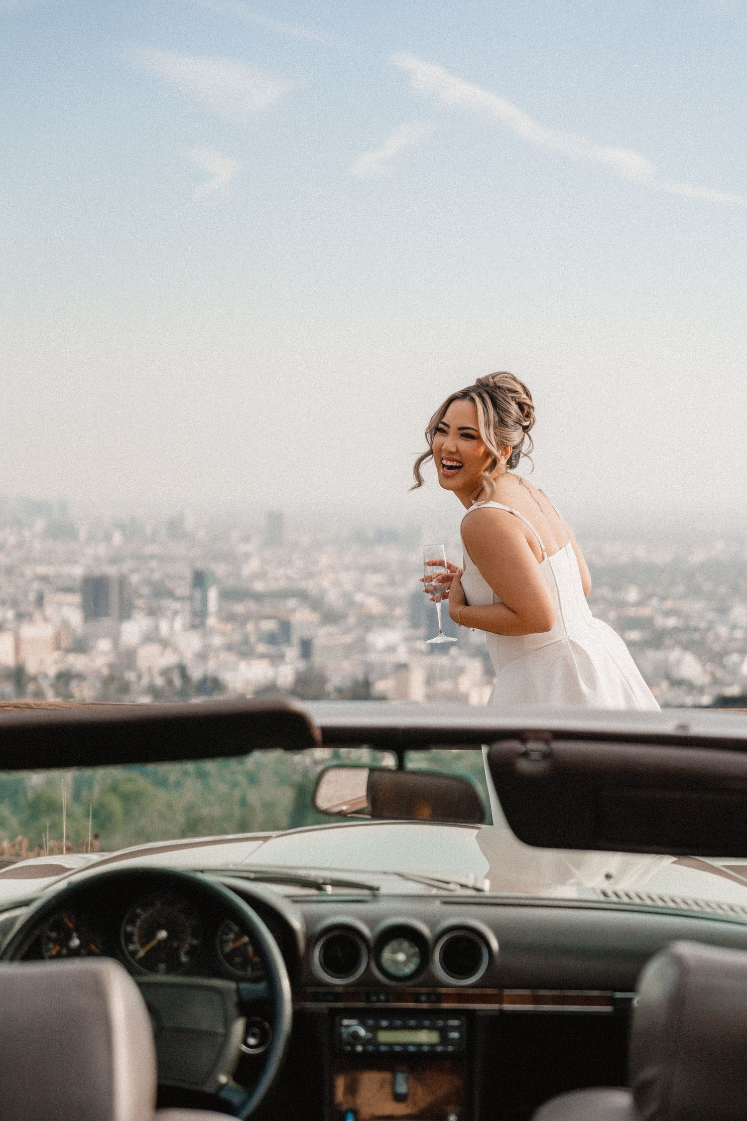 Bride-to-be laughing candidly holding a glass of champagne with a view of Hollywood in the background.