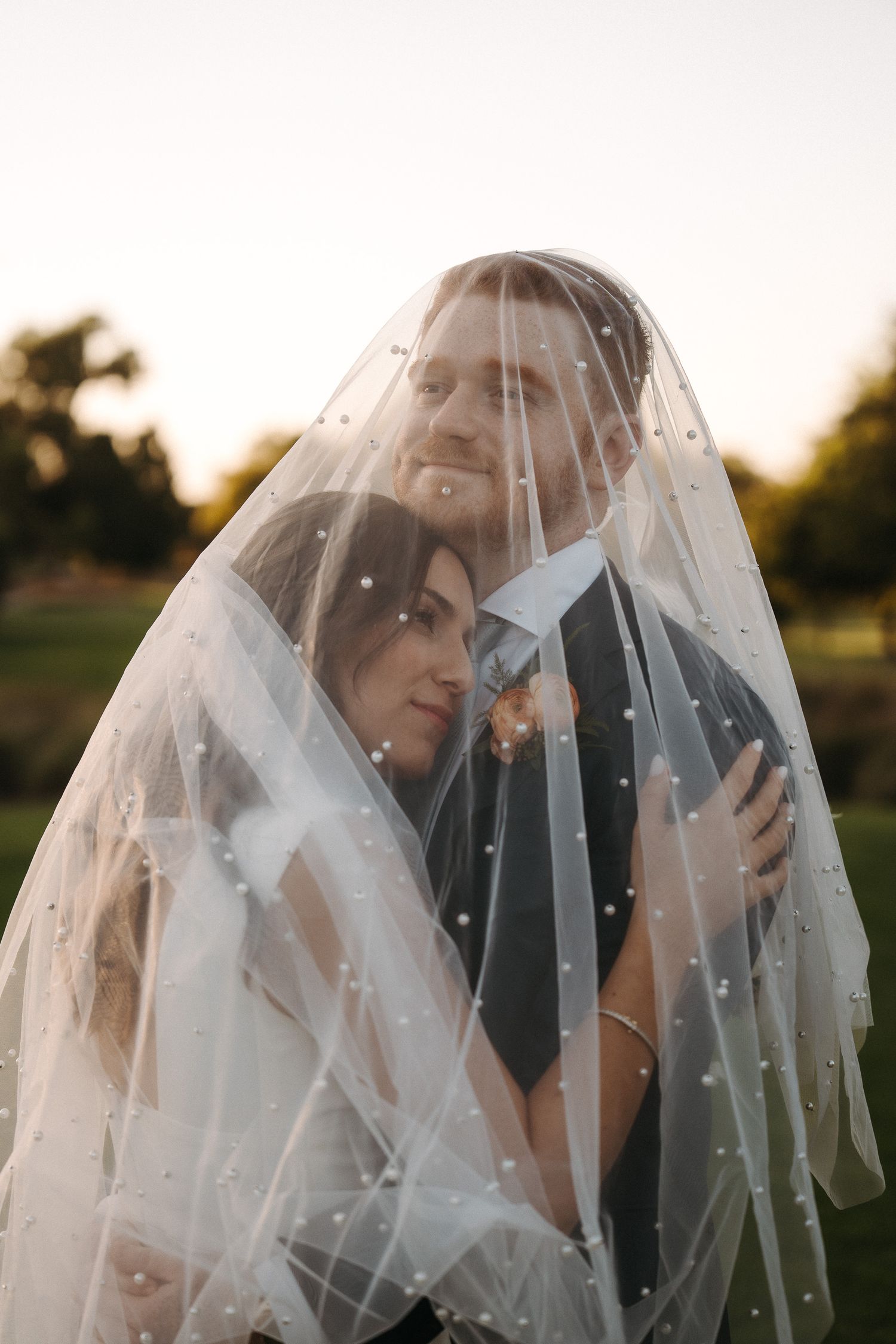 Newlyweds embracing beneath bride's veil during sunset photos on their wedding day.