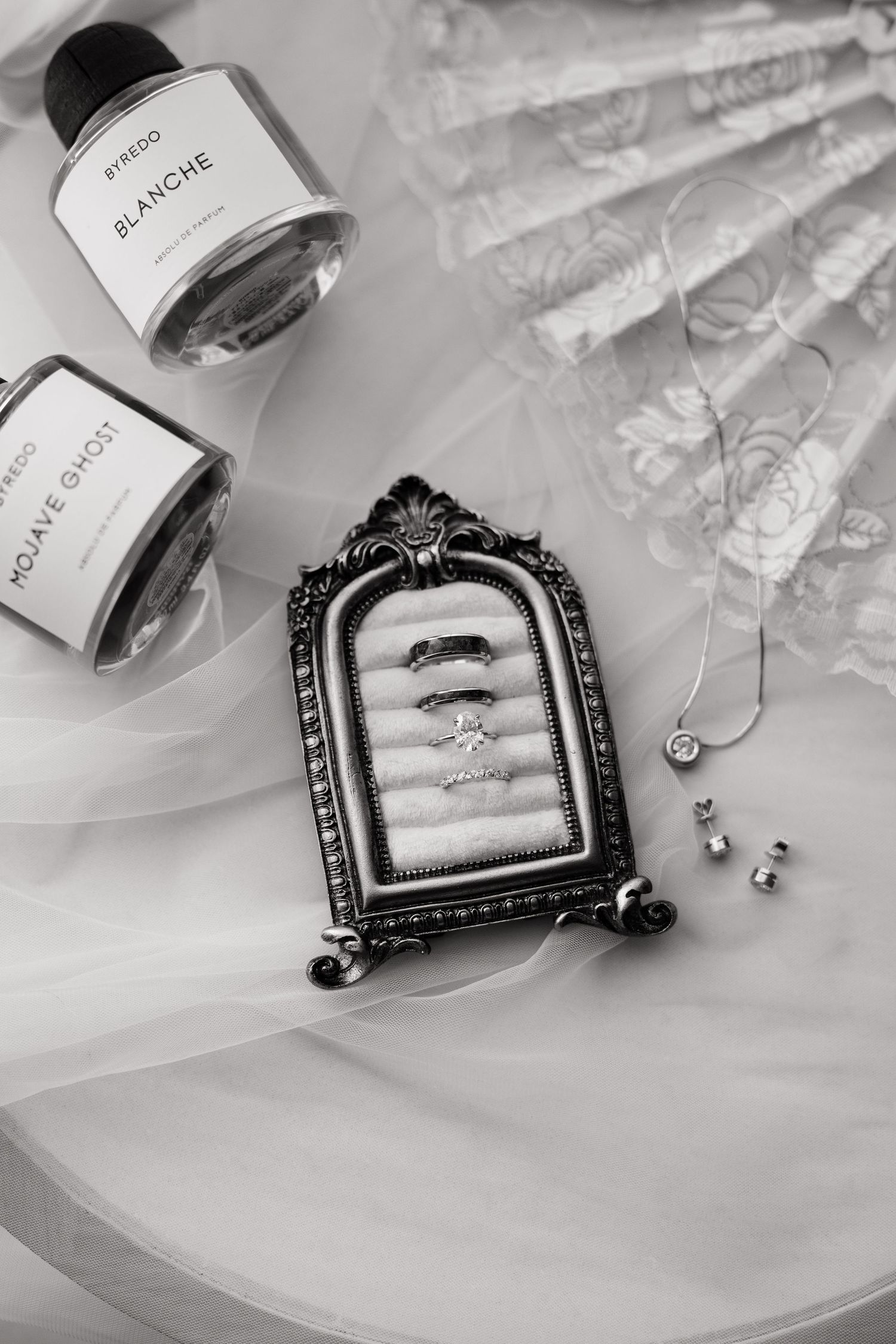 Black and white detail shot with wedding rings and perfume.