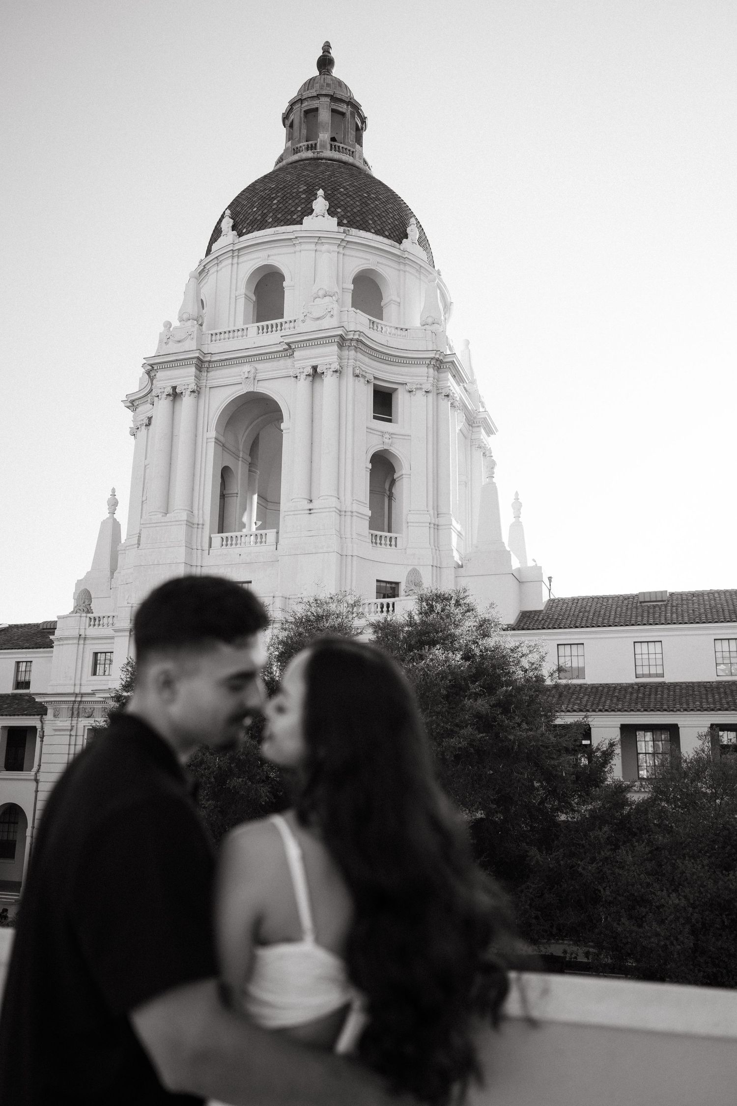 Black and white photo of a couple kissing in front of the iconic Pasadena City Hall dome.