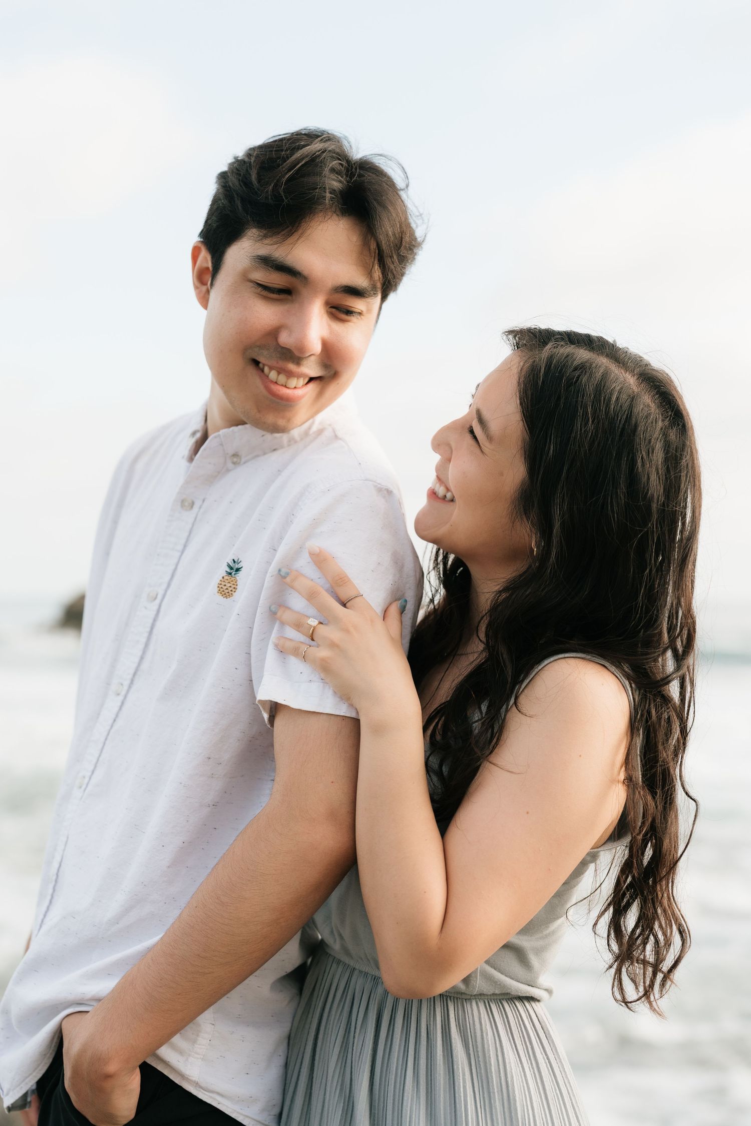 Newly engaged couple smiling with Laguna Beach in the background during their engagement photography session.