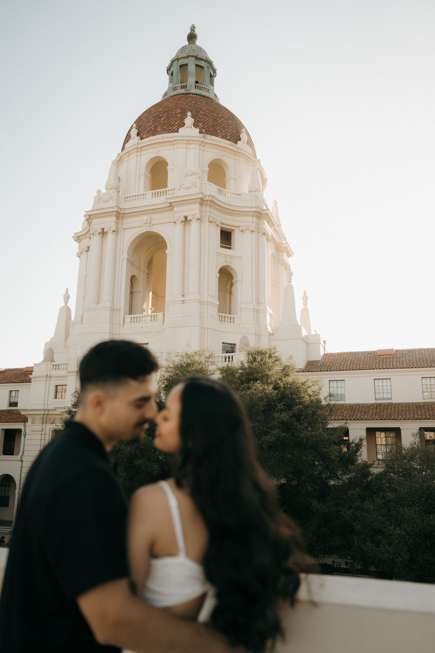 Couple sharing a romantic kiss in front of the iconic Pasadena City Hall dome at golden hour.